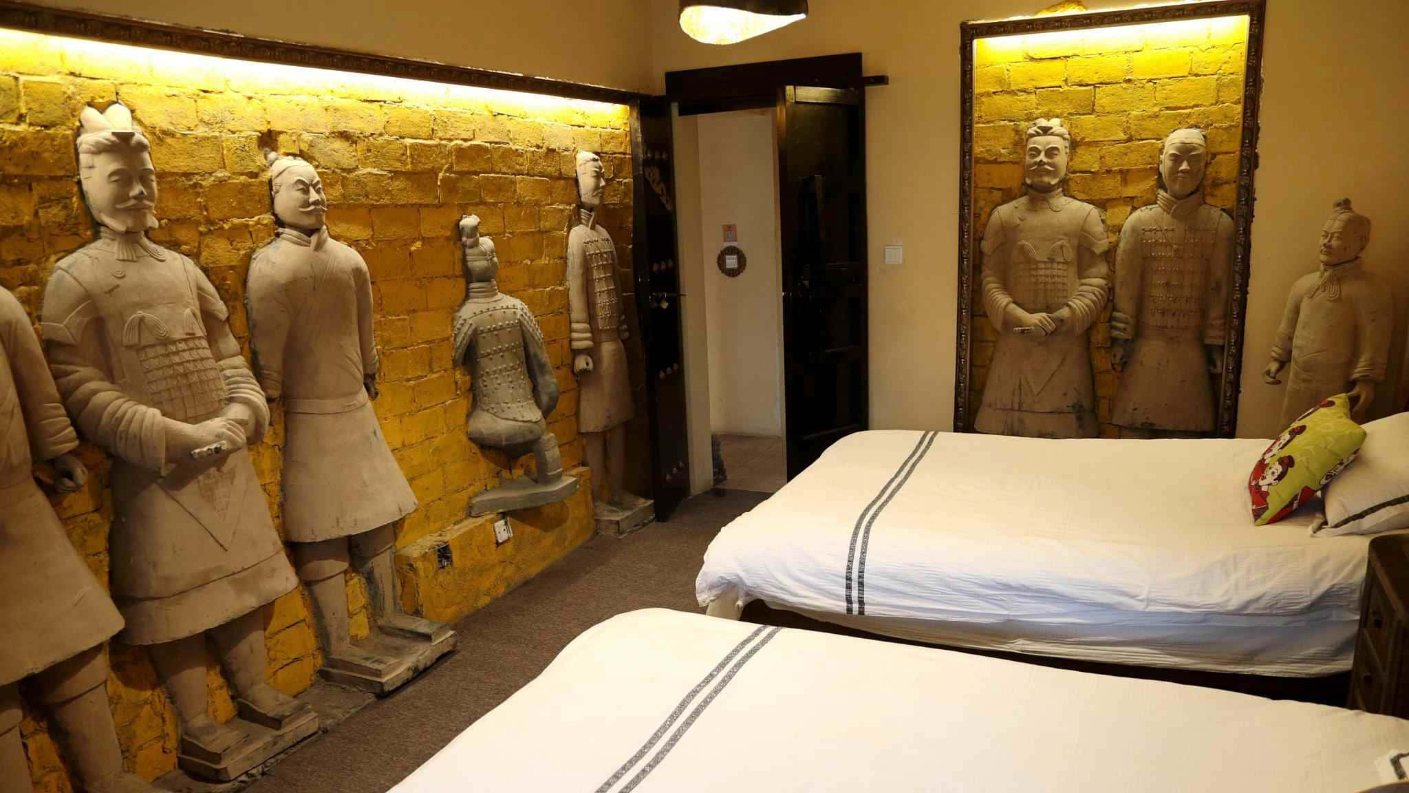 Museum 桌布 壁紙 — 一間酒店房間，黃色磚牆上安裝了兵馬俑雕像，旁邊有兩張床。