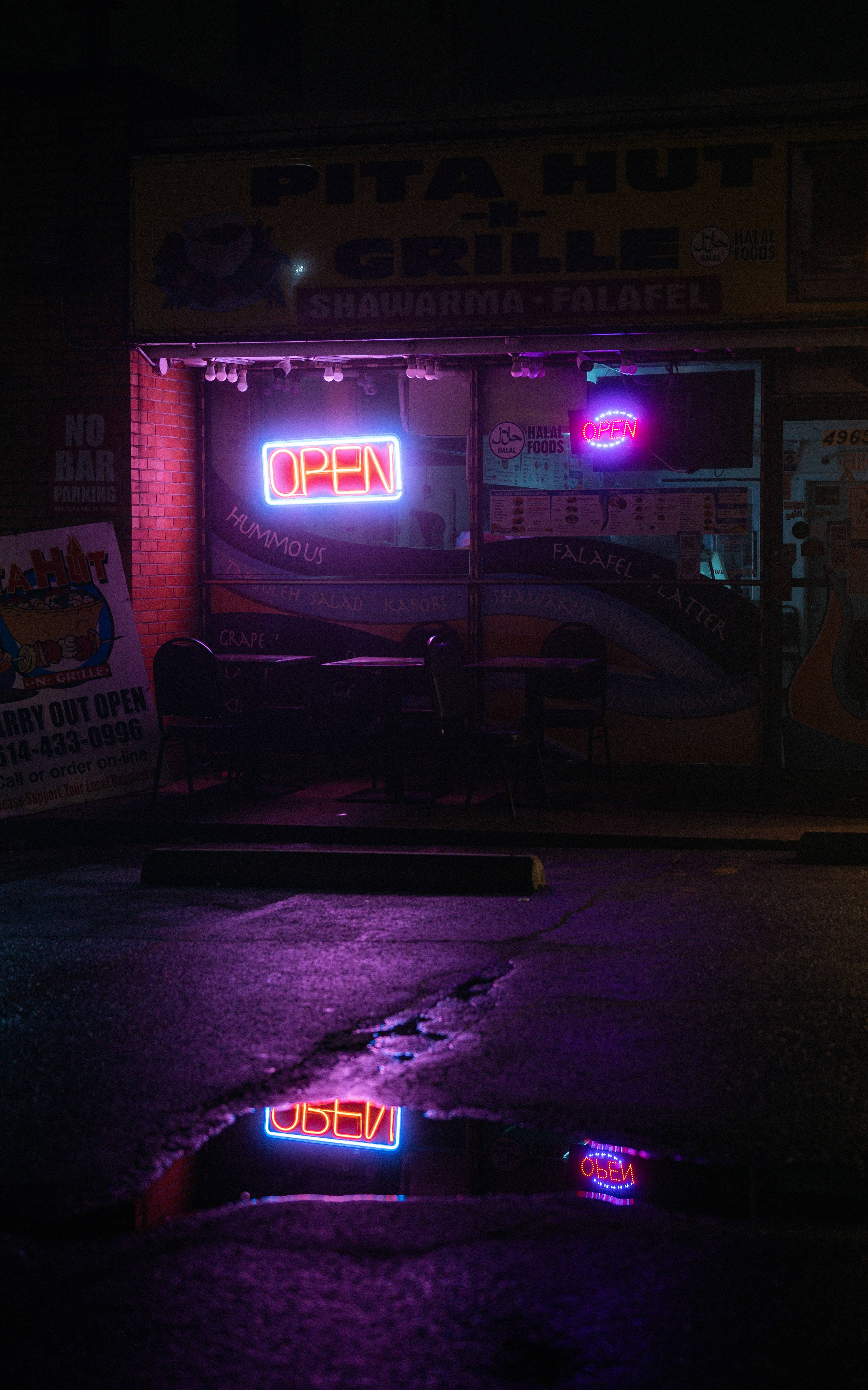 neon sign 桌布 壁紙 — 一間霓虹燈照亮的皮塔餅餐廳在夜晚，發光的「營業中」標誌倒映在濕漉漉人行道上的水窪中。