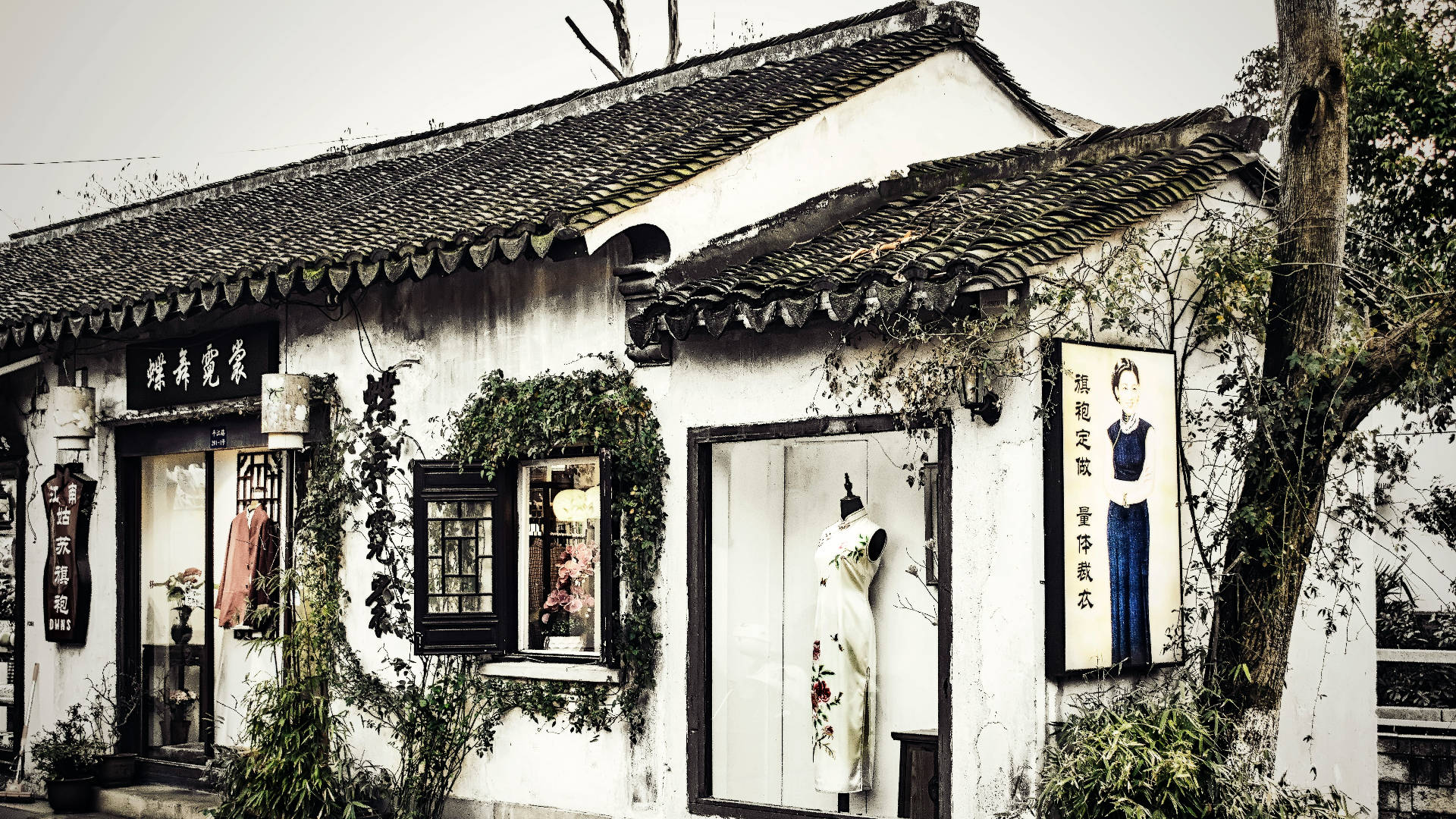 Suzhou 桌布 壁紙 — 一間風化的傳統中式商店，白色牆壁、黑色瓦片屋頂，常春藤攀爬在外牆上，天空多雲。