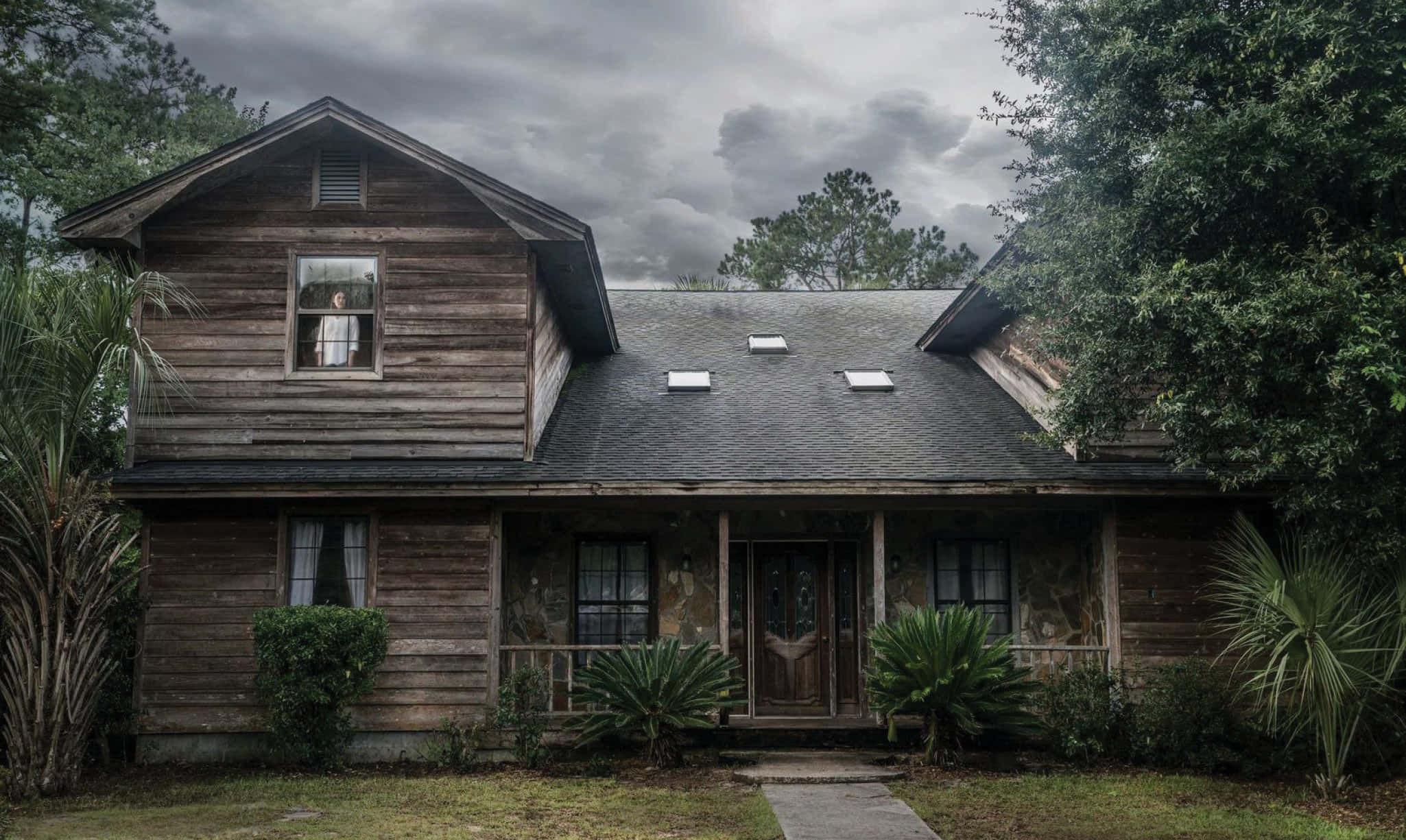 Haunted House 桌布 壁紙 — 一間風化的木屋，深色屋頂，陰沉天空下，上層窗戶有人影窺視。