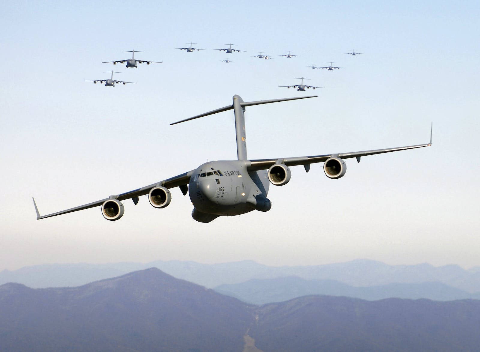 Air Force 桌布 壁紙 — 一隊灰色軍用運輸機在淡藍色天空下，以精確編隊飛越山脈。