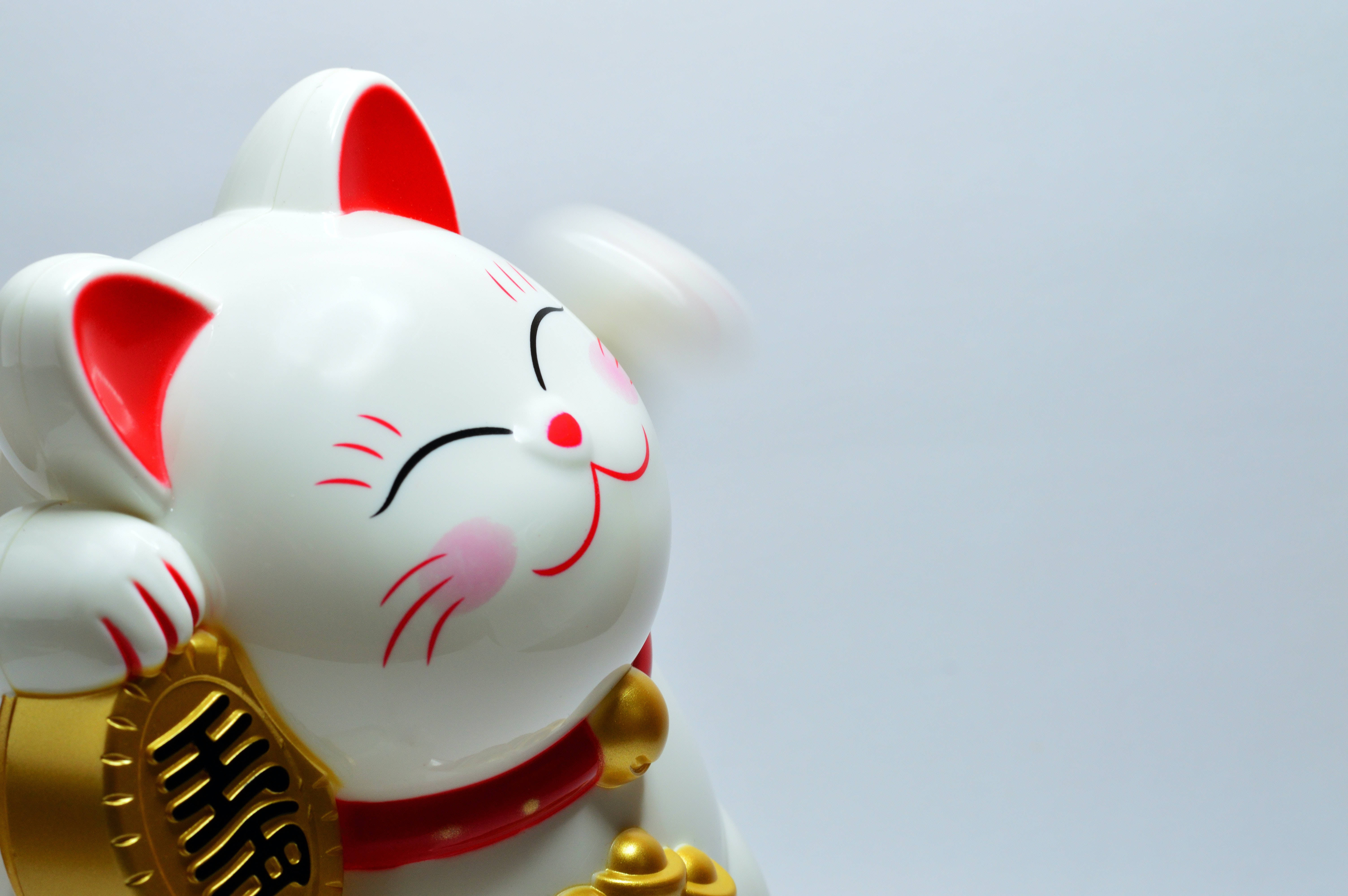 平板電腦 桌布 壁紙 — 一隻亮面白色招財貓公仔，帶有紅色點綴和金幣，在純淺灰色背景上保持微笑姿勢。