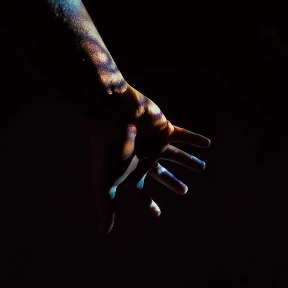 Dark Hand 桌布 壁紙 — 一隻人類的手和前臂在漆黑的背景下發出彩虹般的光芒。