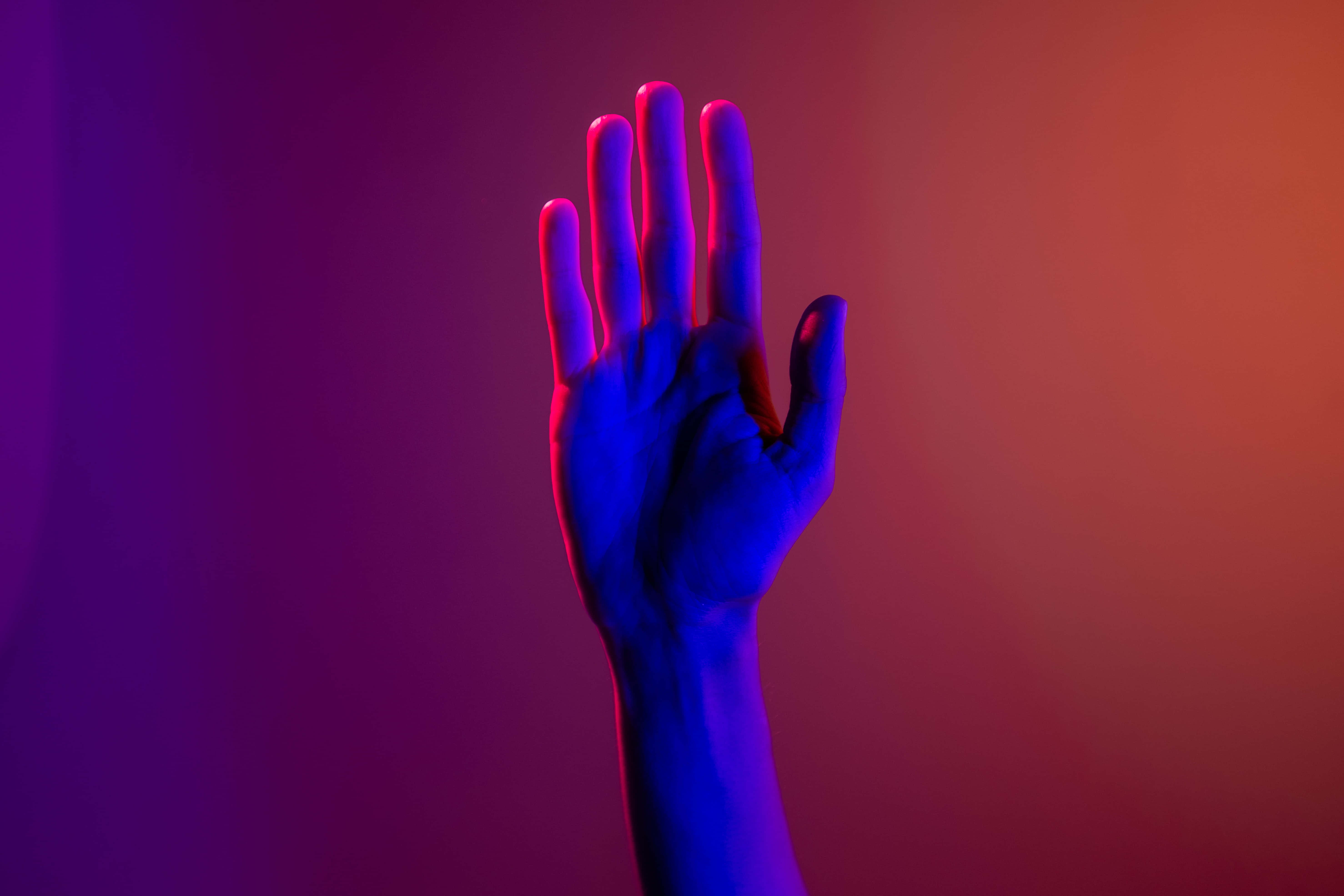 hands 桌布 壁紙 — 一隻人類的手在霓虹燈光照耀的漸變紫色和橙色背景前舉起。