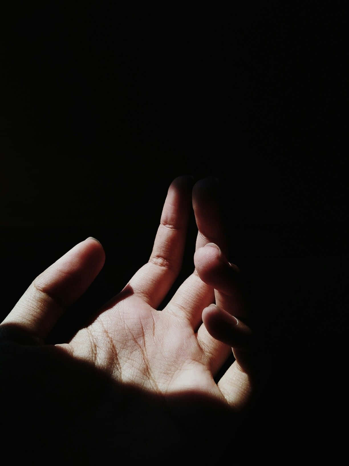 Dark Hand 桌布 壁紙 — 一隻人類的手在黑暗中向上伸展，手指微微張開，被一道光束照亮，突顯皮膚紋理和靜脈。