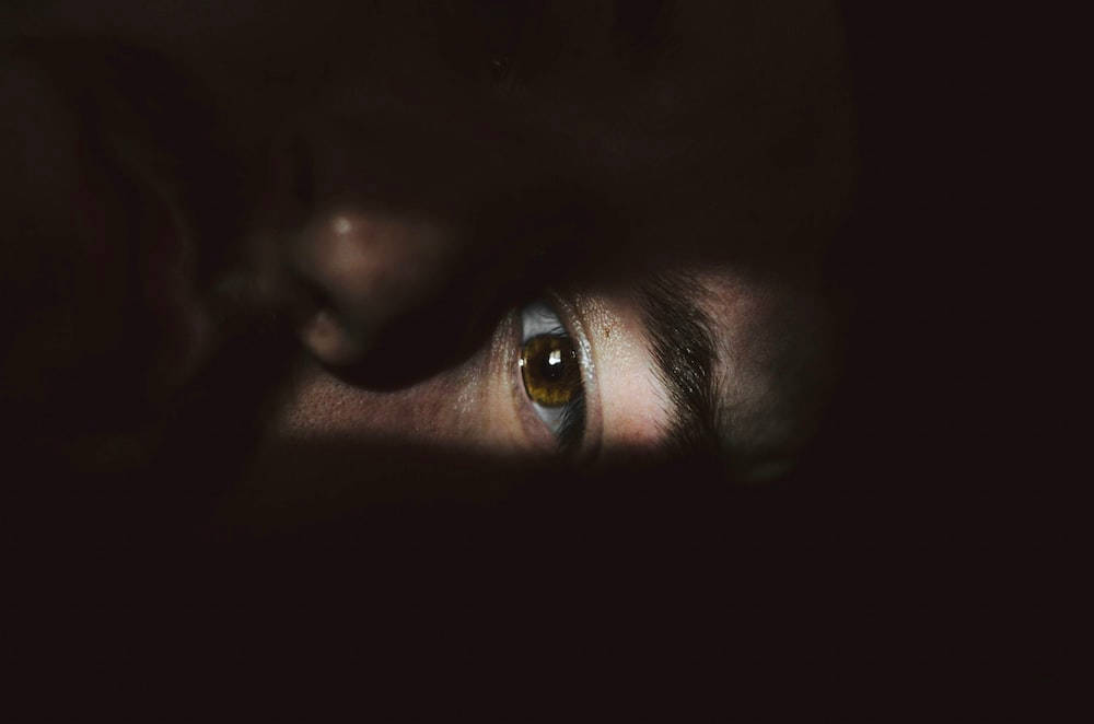 Eye 桌布 壁紙 — 一隻人類眼睛在近乎黑暗中發出琥珀色光芒，帶有戲劇性的明暗對比照明。
