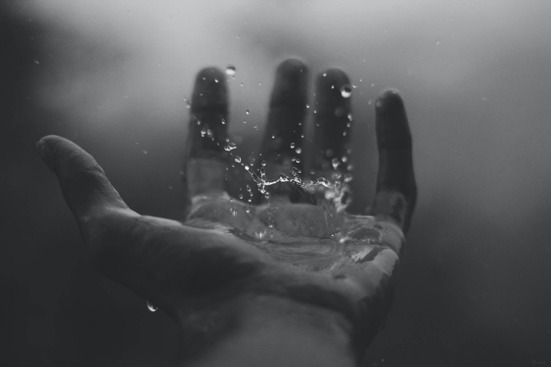 hand 桌布 壁紙 — 一隻伸出的手在水下的單色特寫，水滴飛濺，光線穿透渾濁的深處。