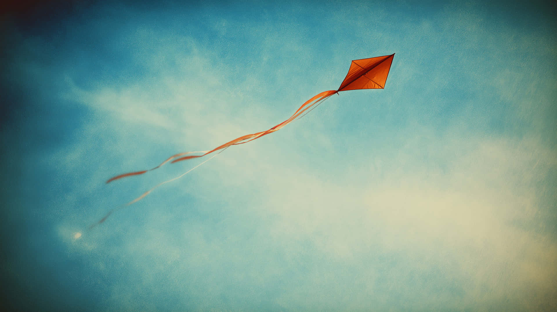 Red Diamond Kite Flying High Against a Bright Blue Sky 壁紙 — 一隻充滿活力的橙色菱形風箏，帶著飄逸的絲帶，在帶有柔和白色雲朵的紋理藍天中優雅地翱翔。