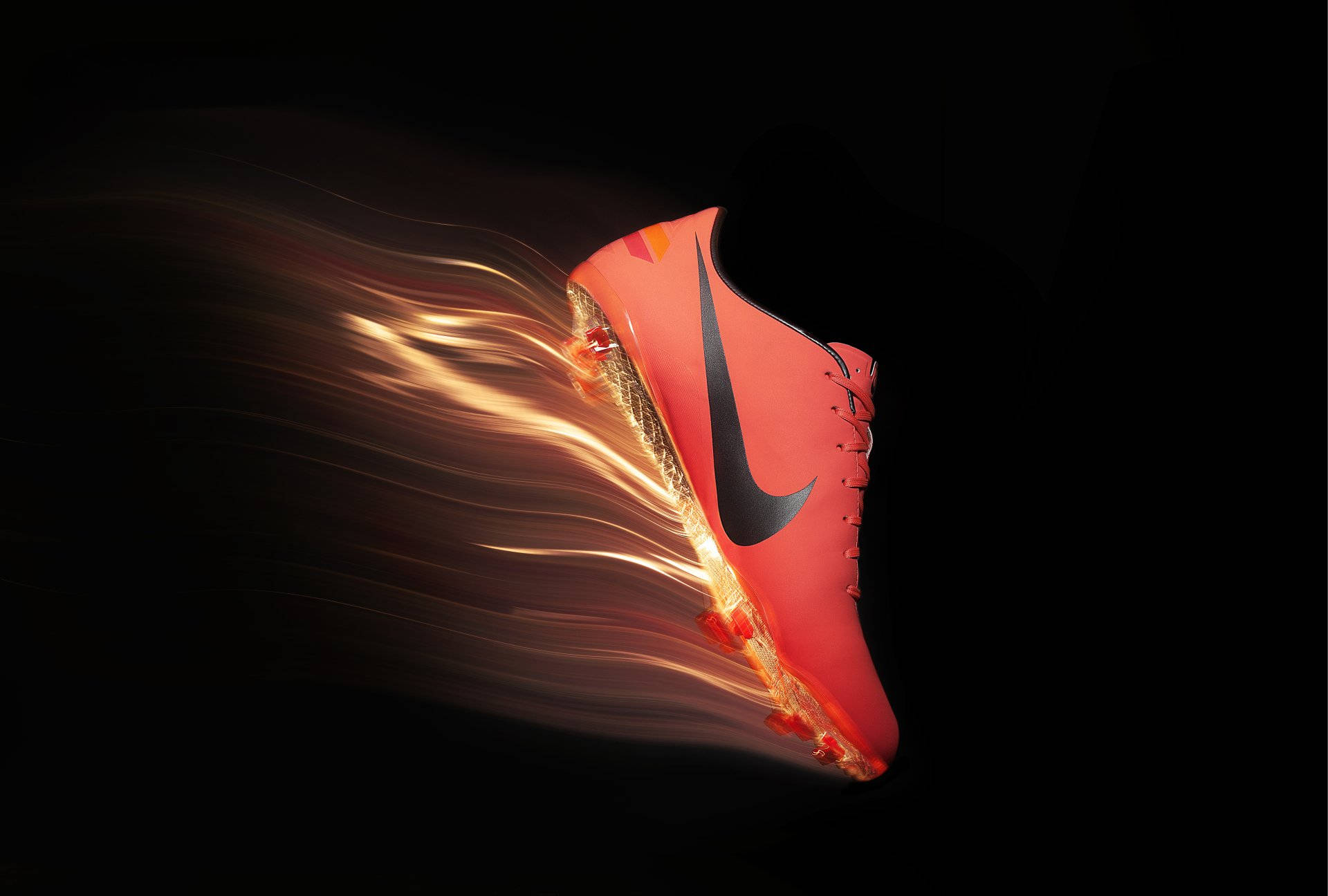 Swoosh 桌布 壁紙 — 一隻充滿活力的橙色足球鞋在黑暗中疾馳，金色動態模糊軌跡強調高速運動。