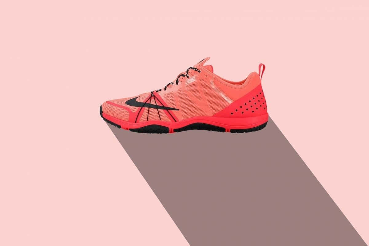 Red Nike 桌布 壁紙 — 一隻充滿活力的珊瑚色Nike訓練鞋在柔和的粉紅色背景上投下長長的陰影，呈現極簡數位藝術風格。
