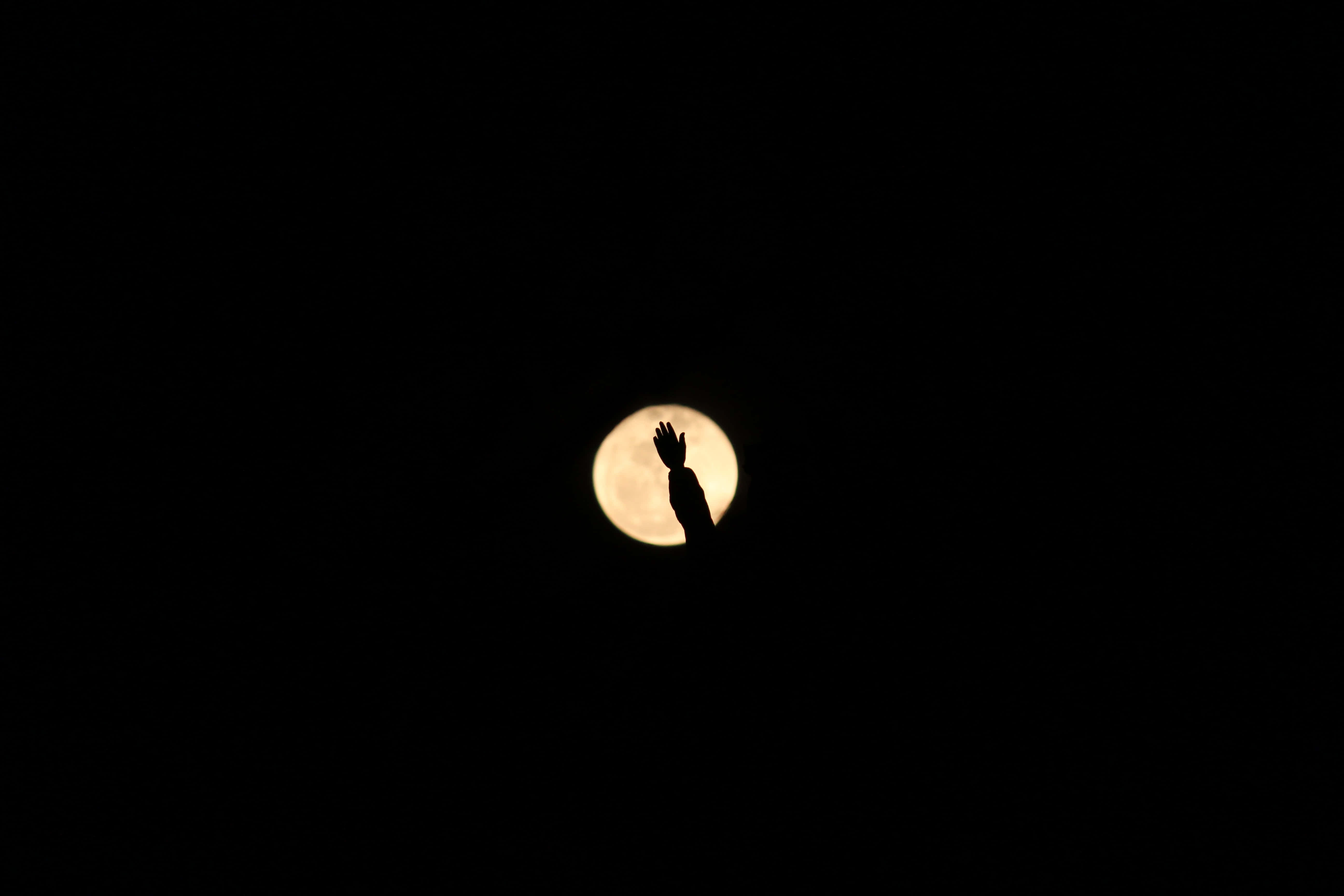Silhouette 桌布 壁紙 — 一隻剪影手向上伸向漆黑天空中發光的滿月。