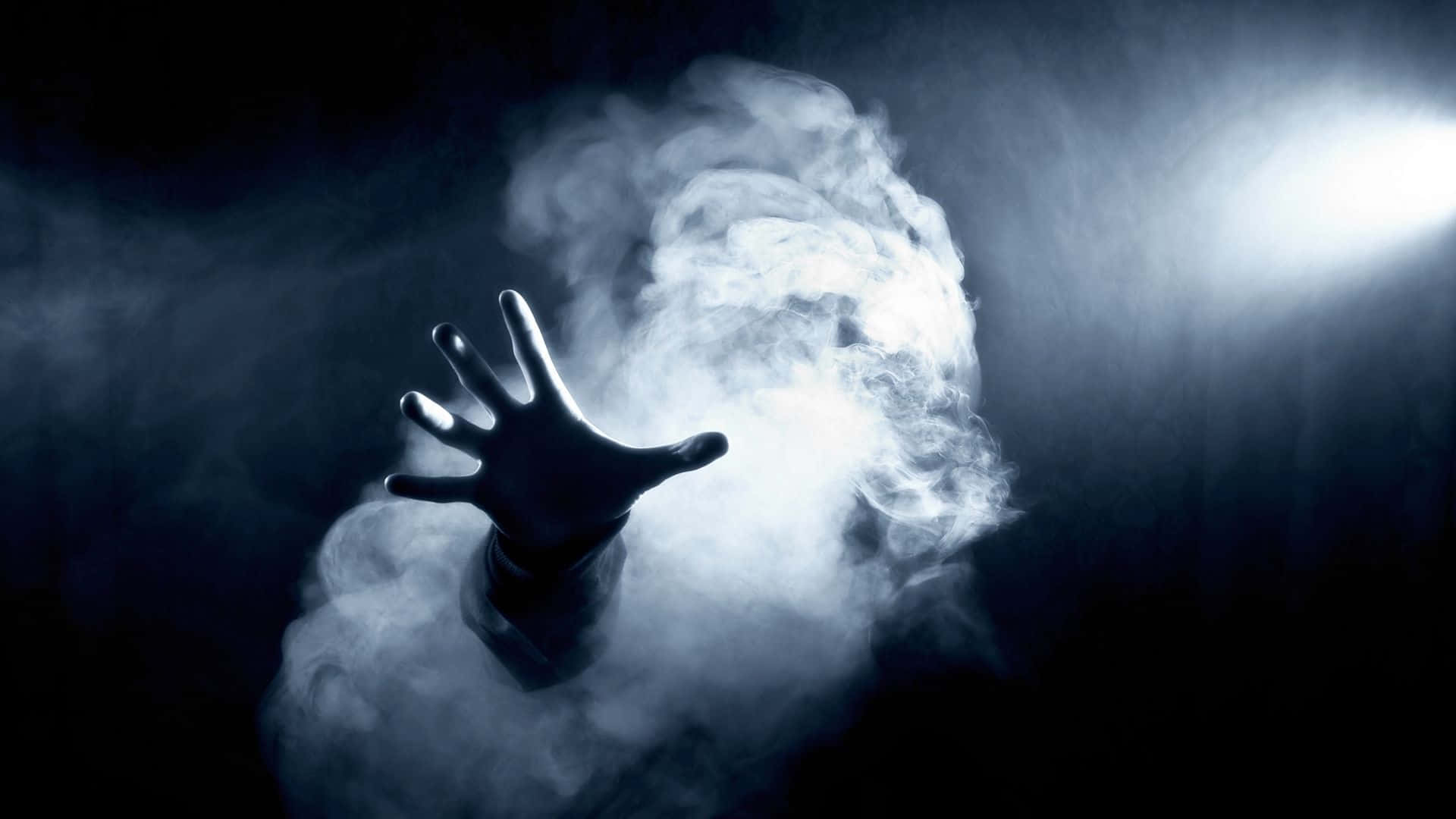 hand 桌布 壁紙 — 一隻剪影手從旋轉的煙霧中浮現，在強烈的聚光燈下，背景黑暗。
