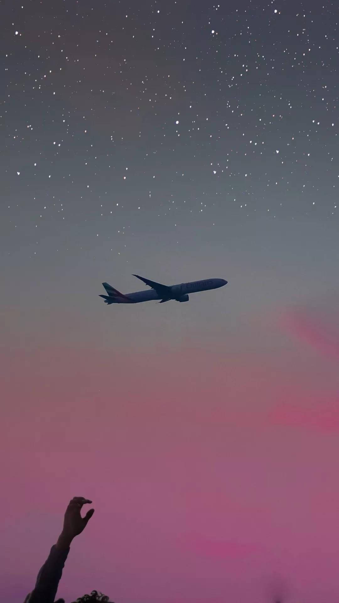 飛機 桌布 壁紙 — 一隻剪影的手伸向繁星點點的暮色天空，一架客機在粉紅色和紫色的雲層上方飛過。