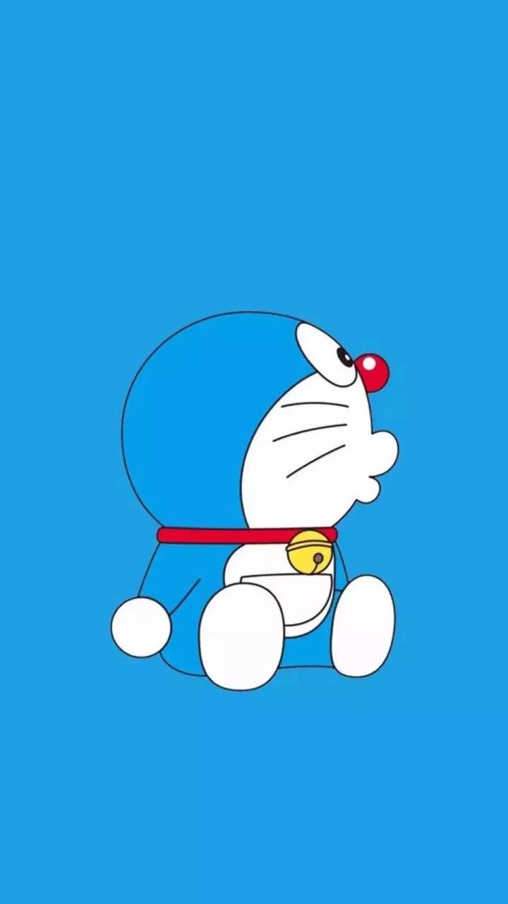 Doraemon 桌布 壁紙 — 一隻卡通機器貓，紅鼻子，掛著鈴鐺，坐在純藍色背景前。