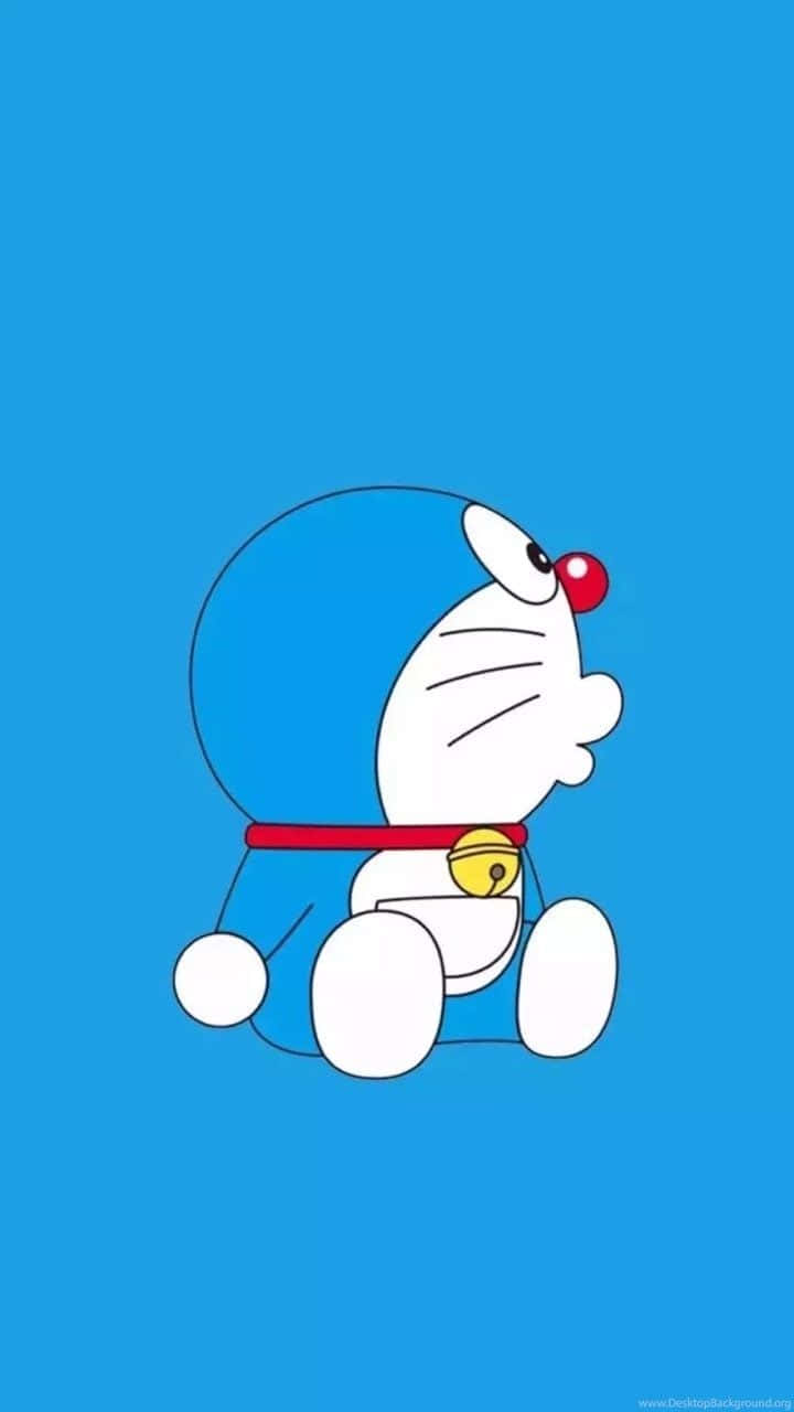 Doraemon 桌布 壁紙 — 一隻卡通機器貓，紅鼻子，掛著鈴鐺，坐在純藍色背景前。