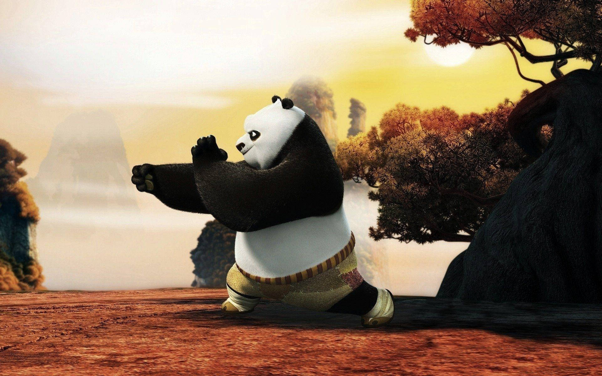 熊貓 桌布 壁紙 — 一隻卡通熊貓在金色日落時分的山徑上擺出武術姿勢，背景有秋樹和霧氣繚繞的山峰。