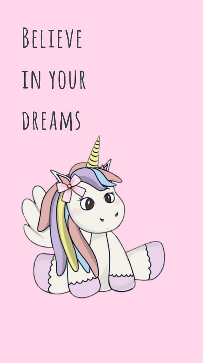 Unicorn Desktop 桌布 壁紙 — 一隻可愛的卡通獨角獸，擁有彩虹鬃毛和角，坐在柔和的粉紅色背景上，下方有文字「相信你的夢想」。
