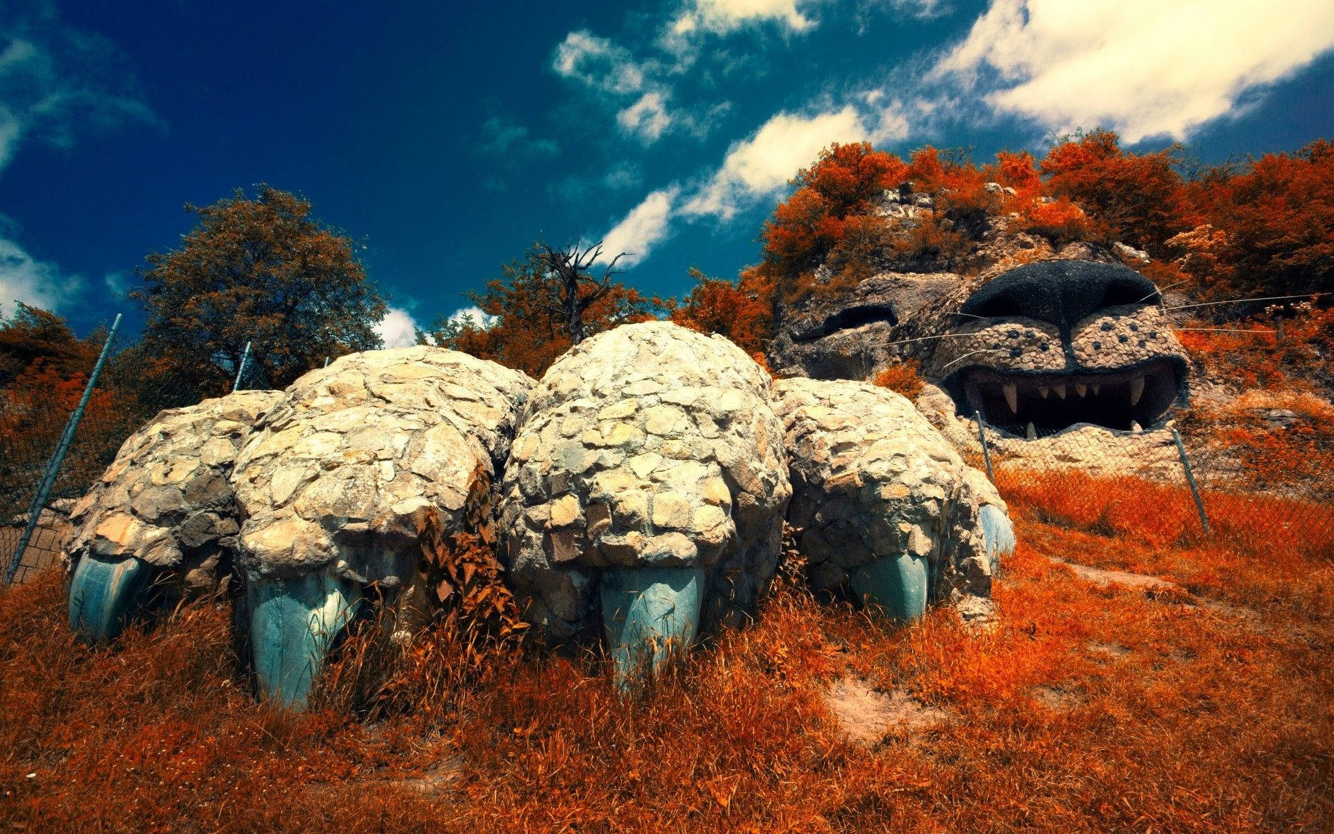 Armenia 桌布 壁紙 — 一隻咆哮的獅子巨型石雕，擁有藍色的爪子和牙齒，矗立在秋日樹木之間，背景是鮮豔的藍天。