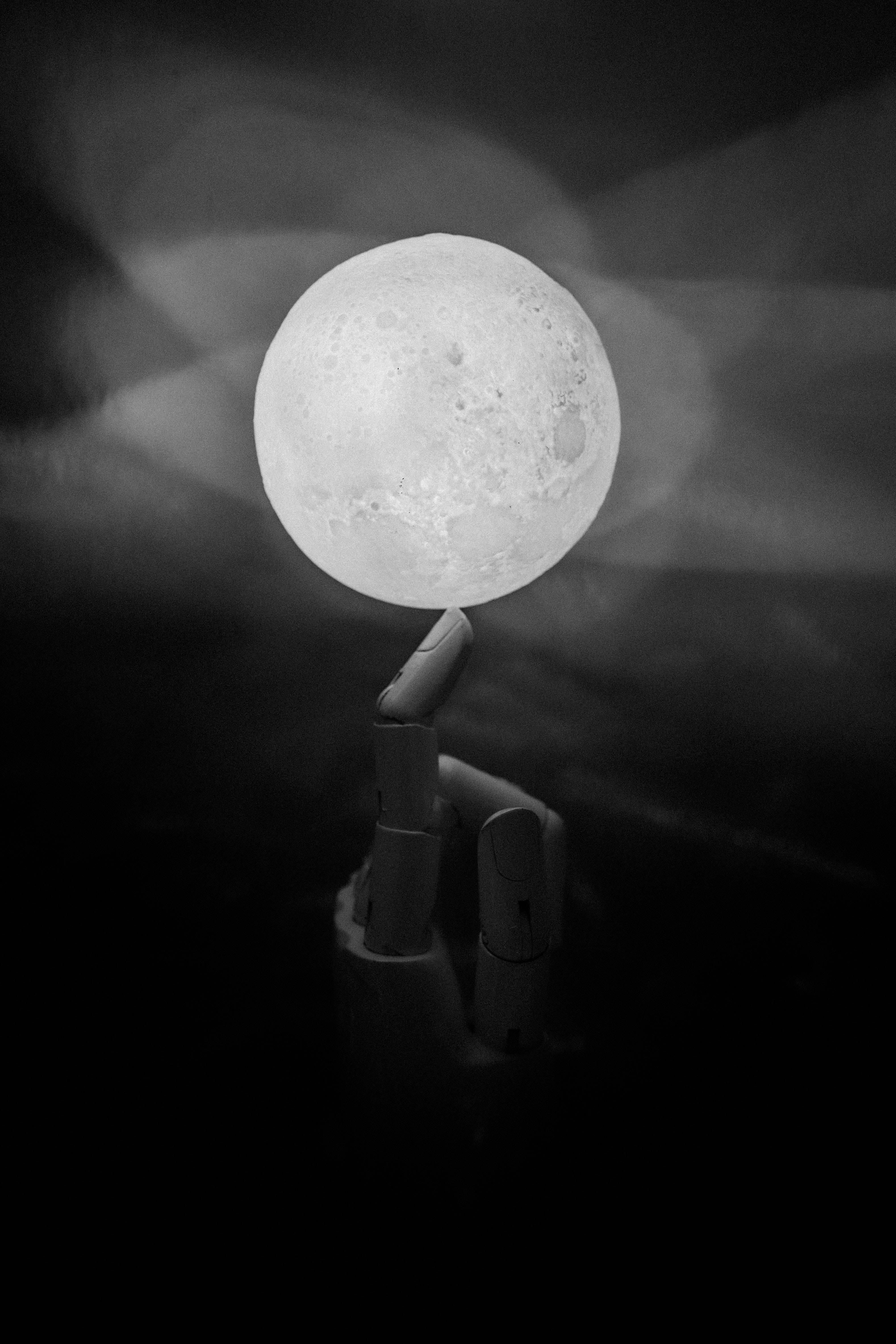 full moon 桌布 壁紙 — 一隻單色手拿著細節豐富的月亮，背景是模糊的黑暗和柔和的光線。