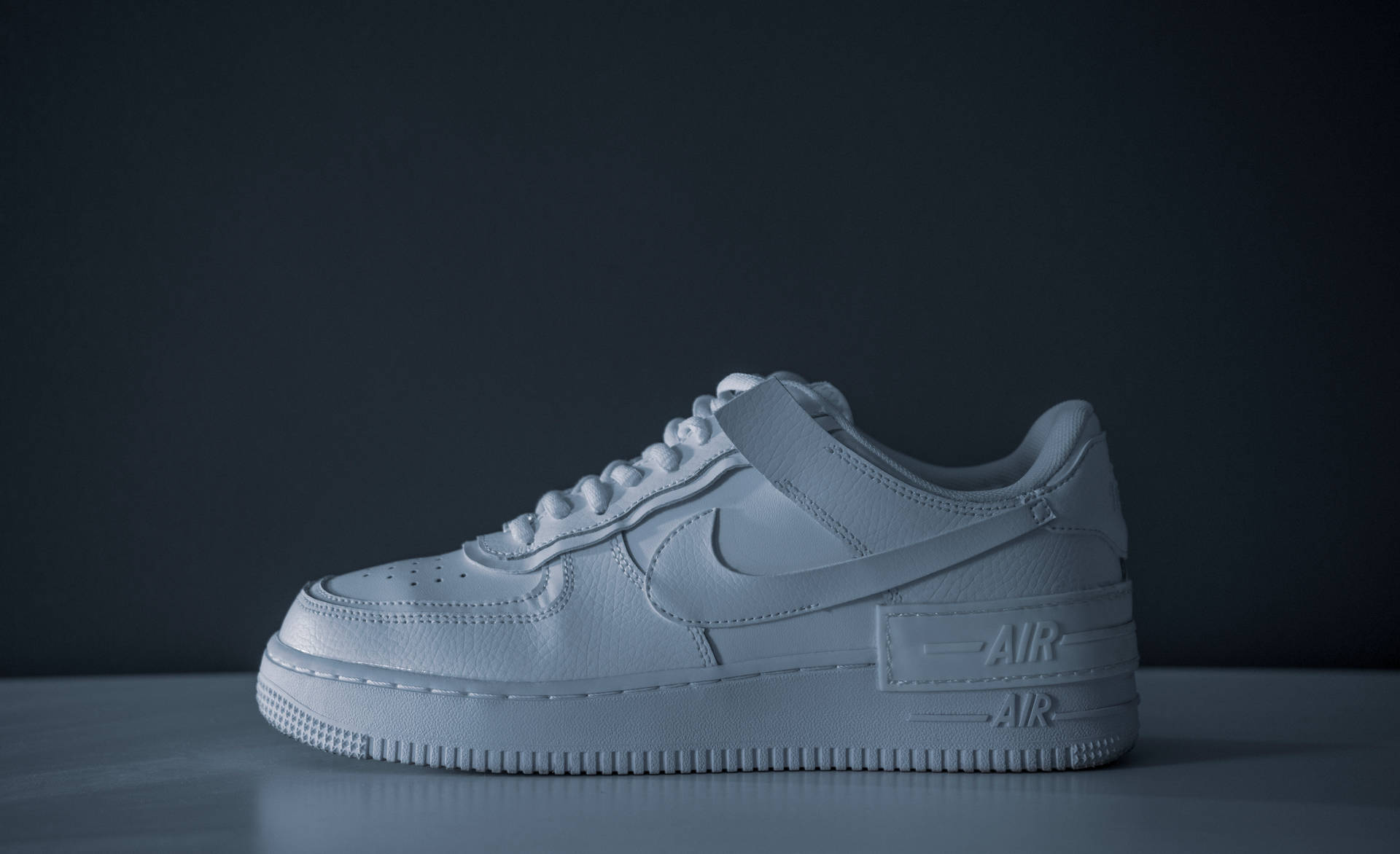 鞋子 桌布 壁紙 — 一隻單色白色Nike Air Force 1運動鞋孤立地放在灰色表面上，背景為深色。