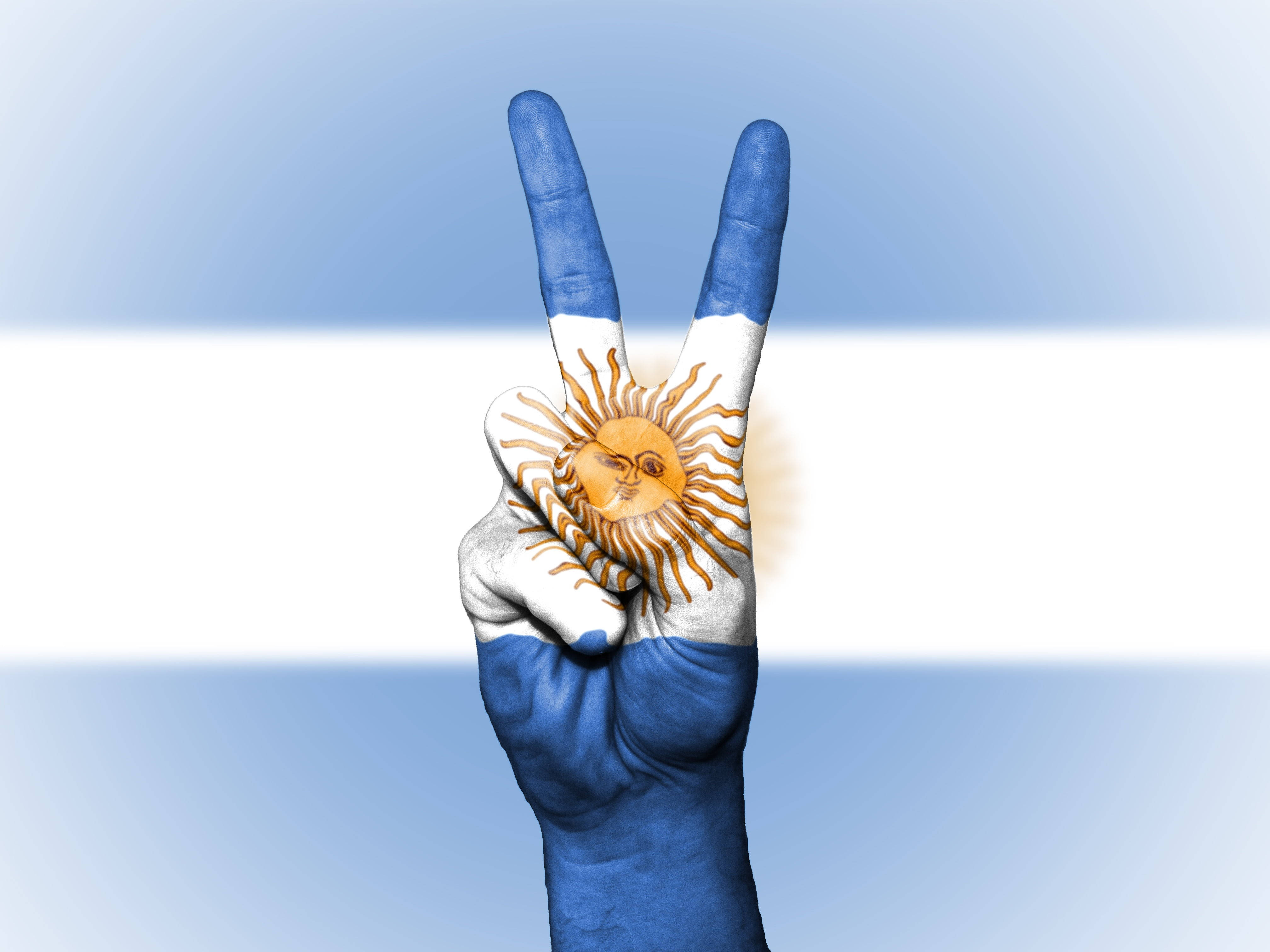 Argentina 桌布 壁紙 — 一隻塗上阿根廷國旗的手在模糊的國旗背景下做出和平手勢。
