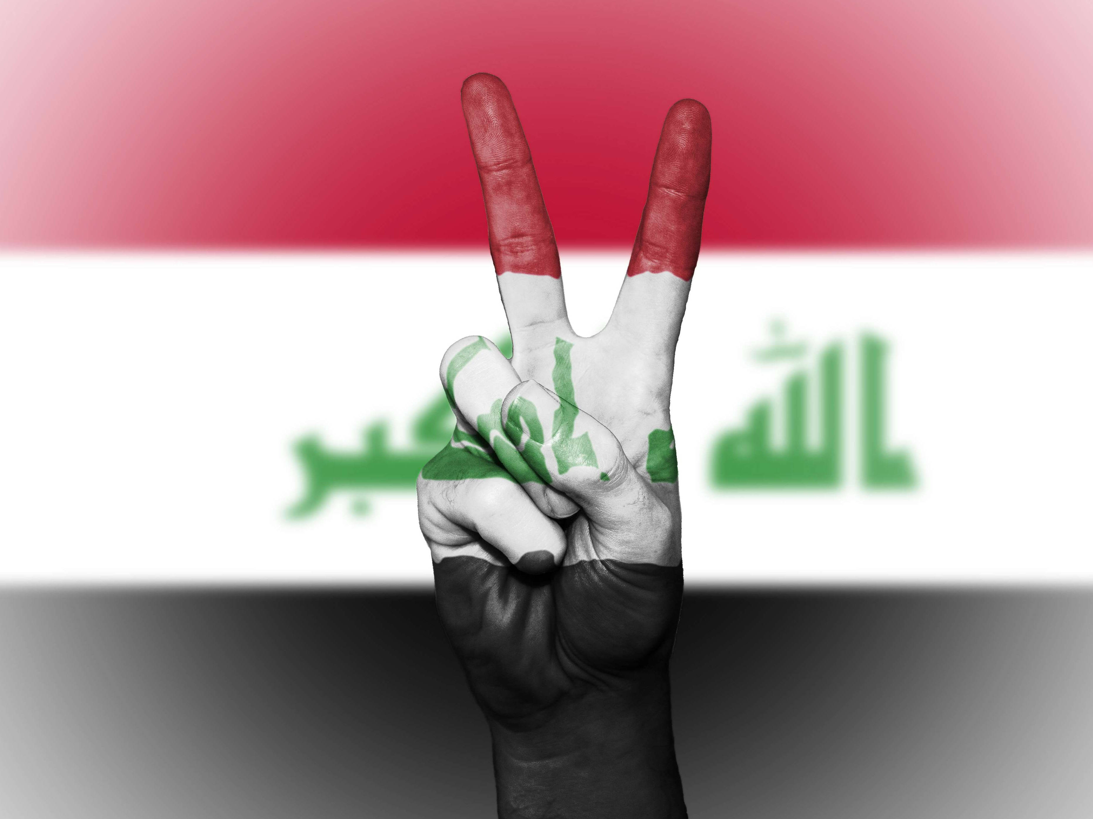 Iraq 桌布 壁紙 — 一隻塗有伊拉克國旗的手在模糊的國旗背景下做出和平手勢。