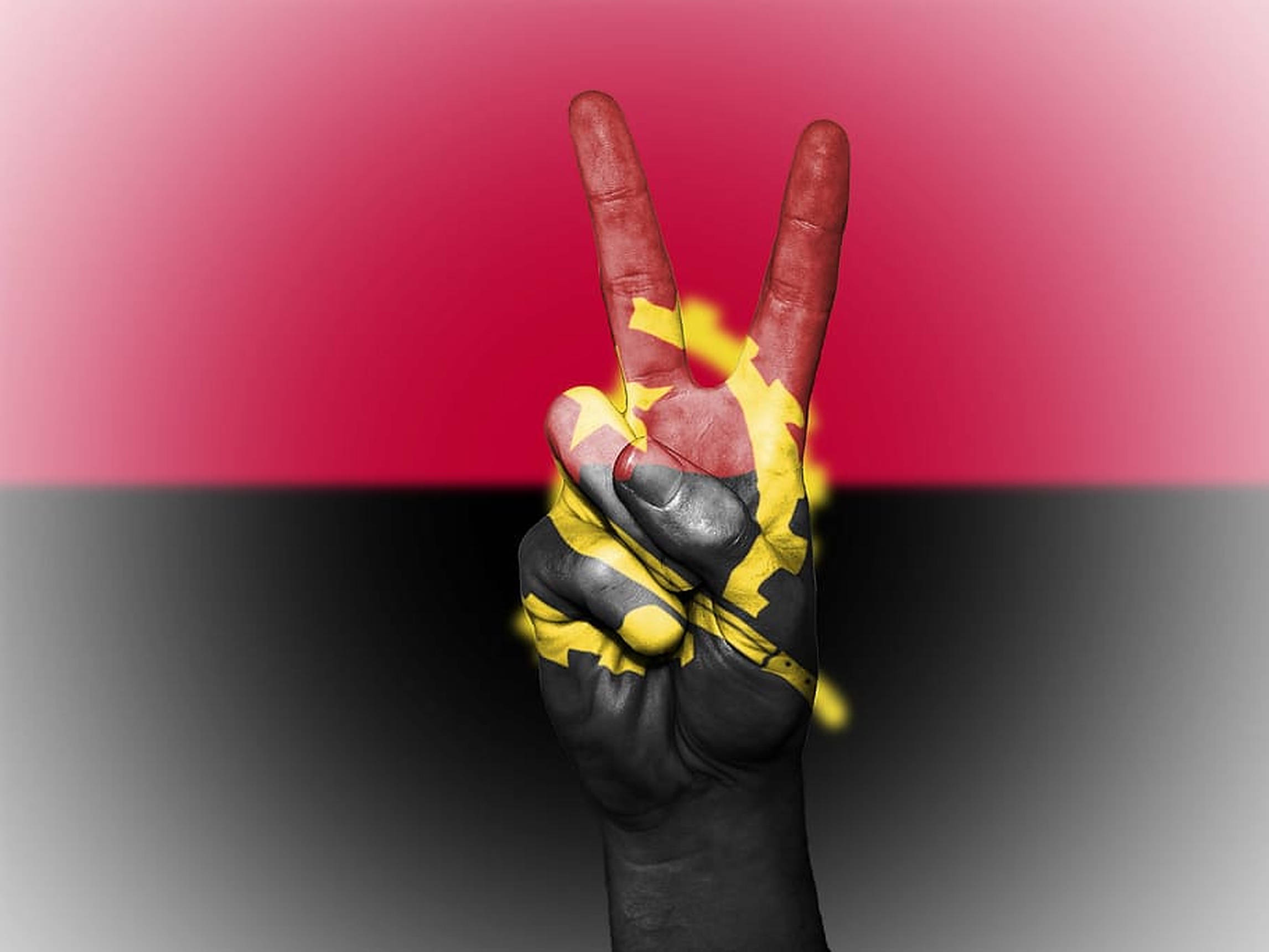 Angola 桌布 壁紙 — 一隻塗有安哥拉國旗的手在紅色和黑色漸變背景上做出和平手勢。