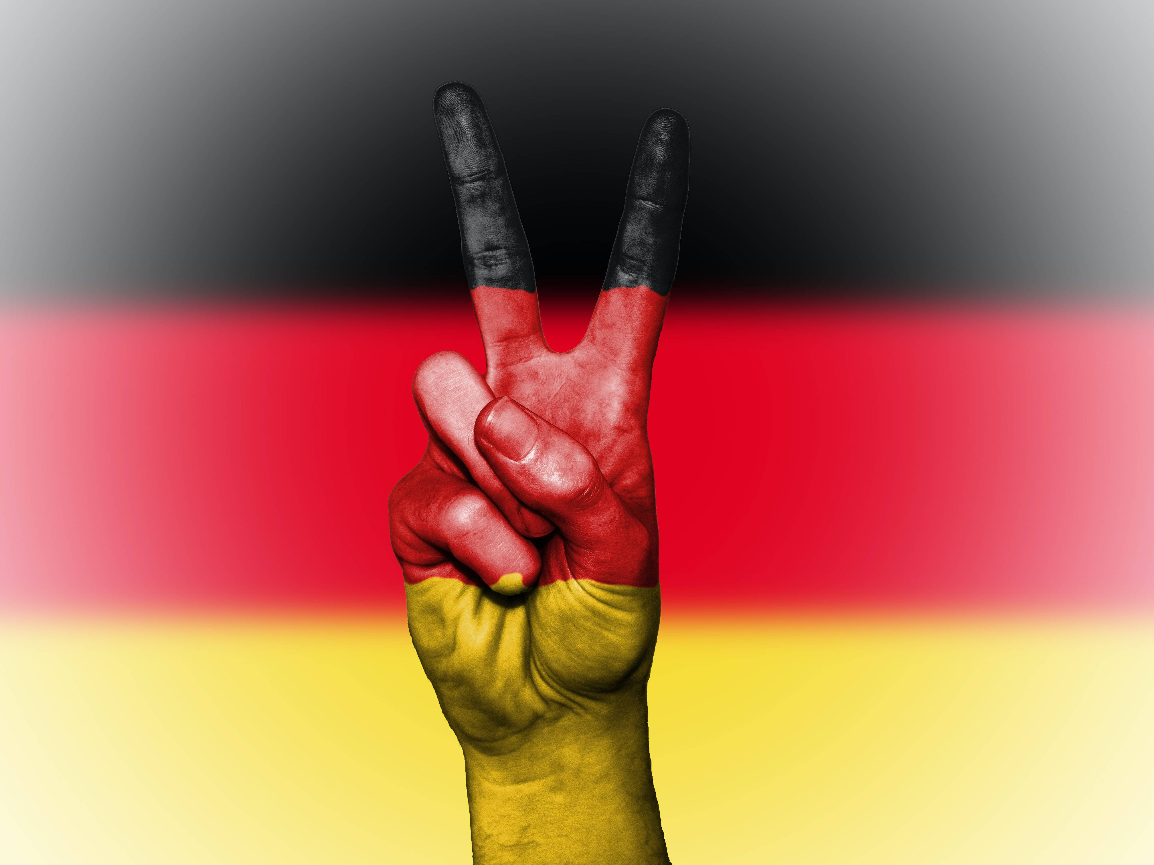 Peace Symbol 桌布 壁紙 — 一隻塗有德國國旗顏色的手在模糊的國旗背景下做出和平手勢。