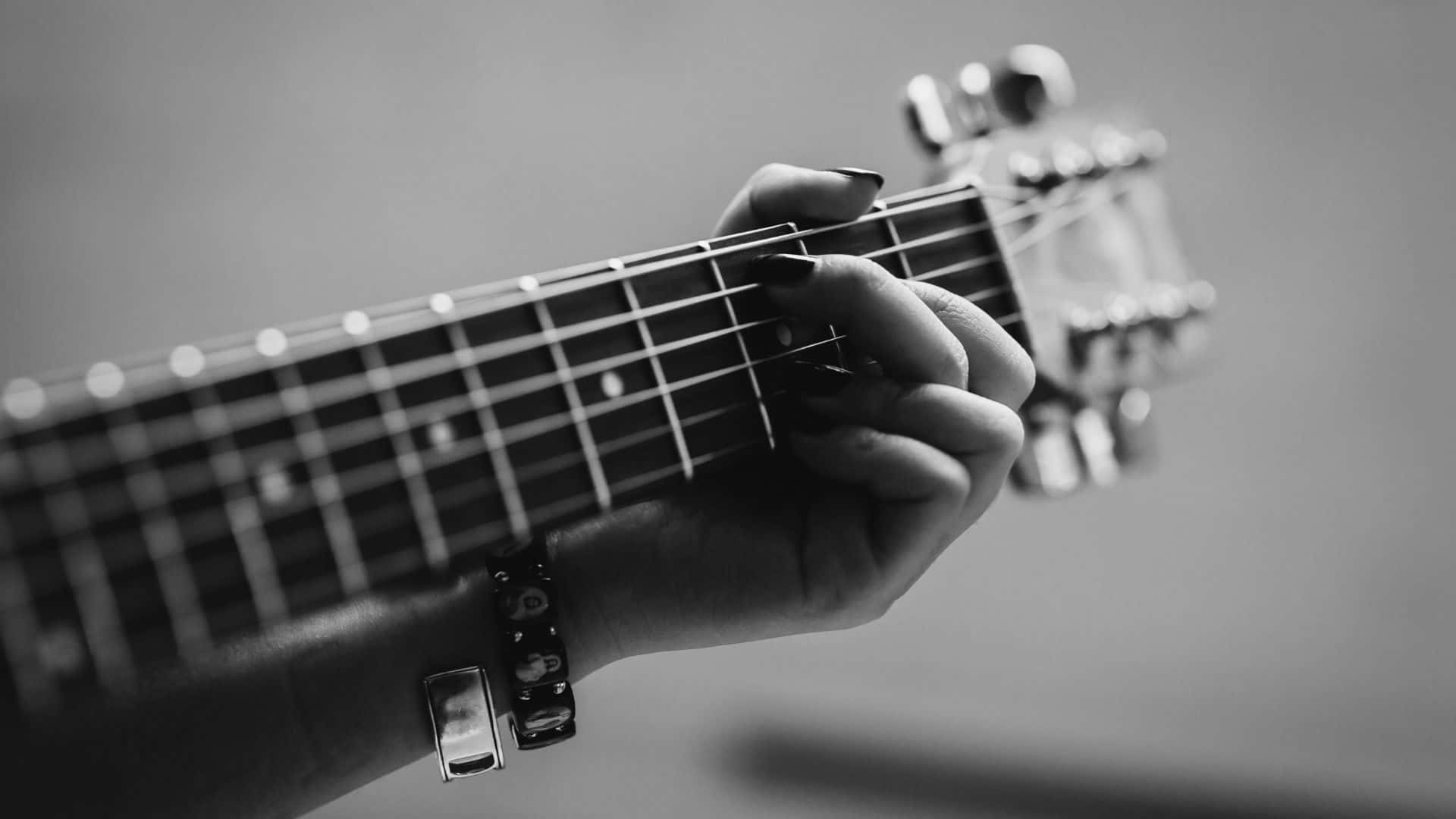 Black And White Guitar 桌布 壁紙 — 一隻塗有深色指甲油的手在單色特寫中按壓吉他琴頸上的琴弦。