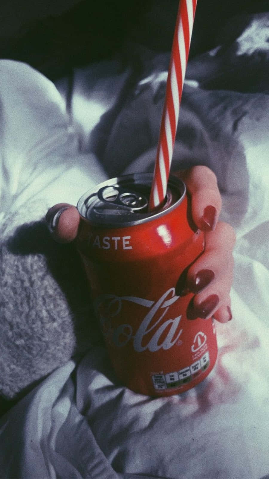 coca cola 桌布 壁紙 — 一隻塗有紅色指甲的手拿著一個紅色可口可樂罐，罐上插著紅白條紋吸管，背景是皺巴巴的白色床單。