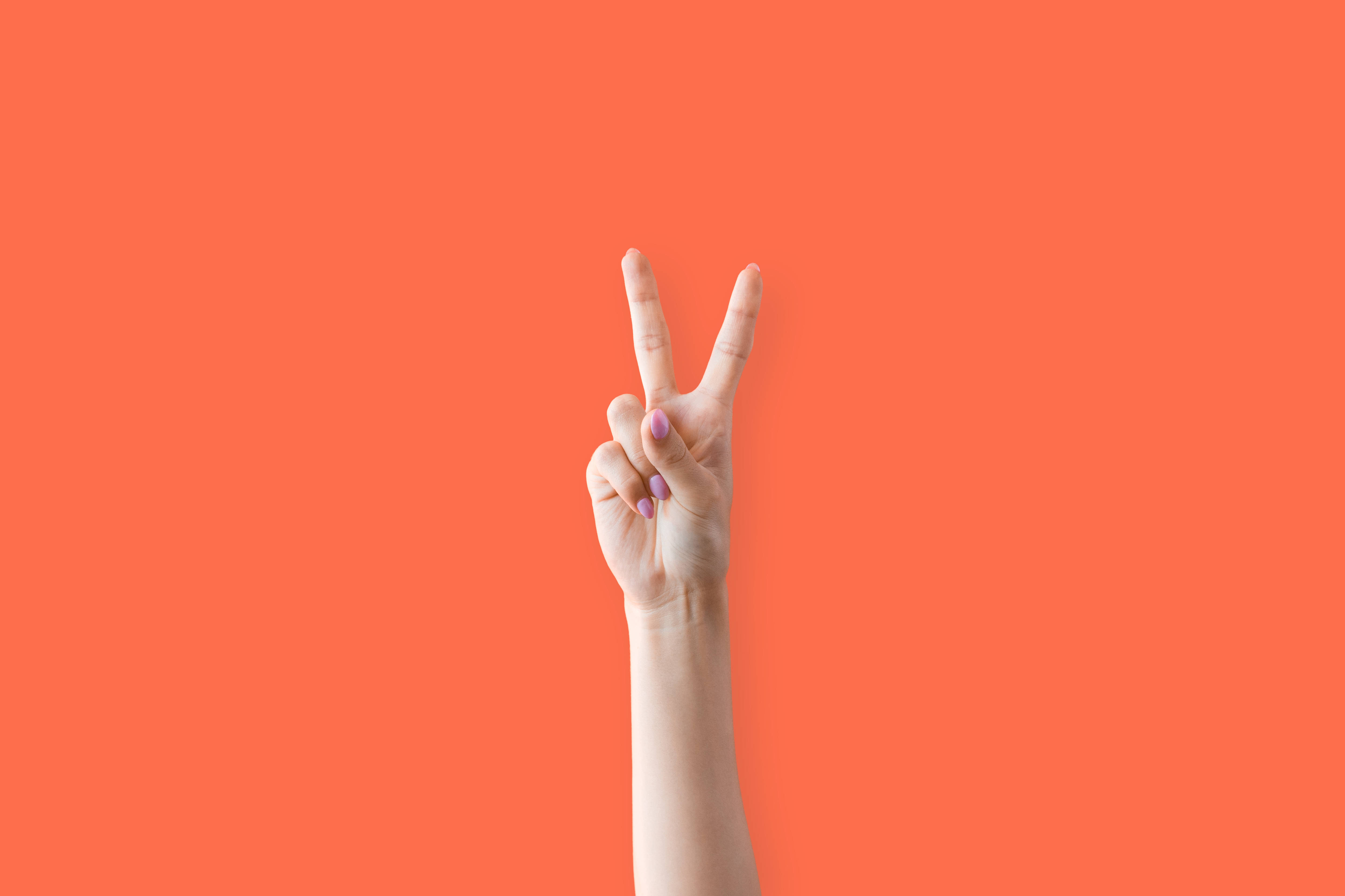 Positive 桌布 壁紙 — 一隻塗有紫色指甲油的手在純珊瑚色背景上做出和平手勢。