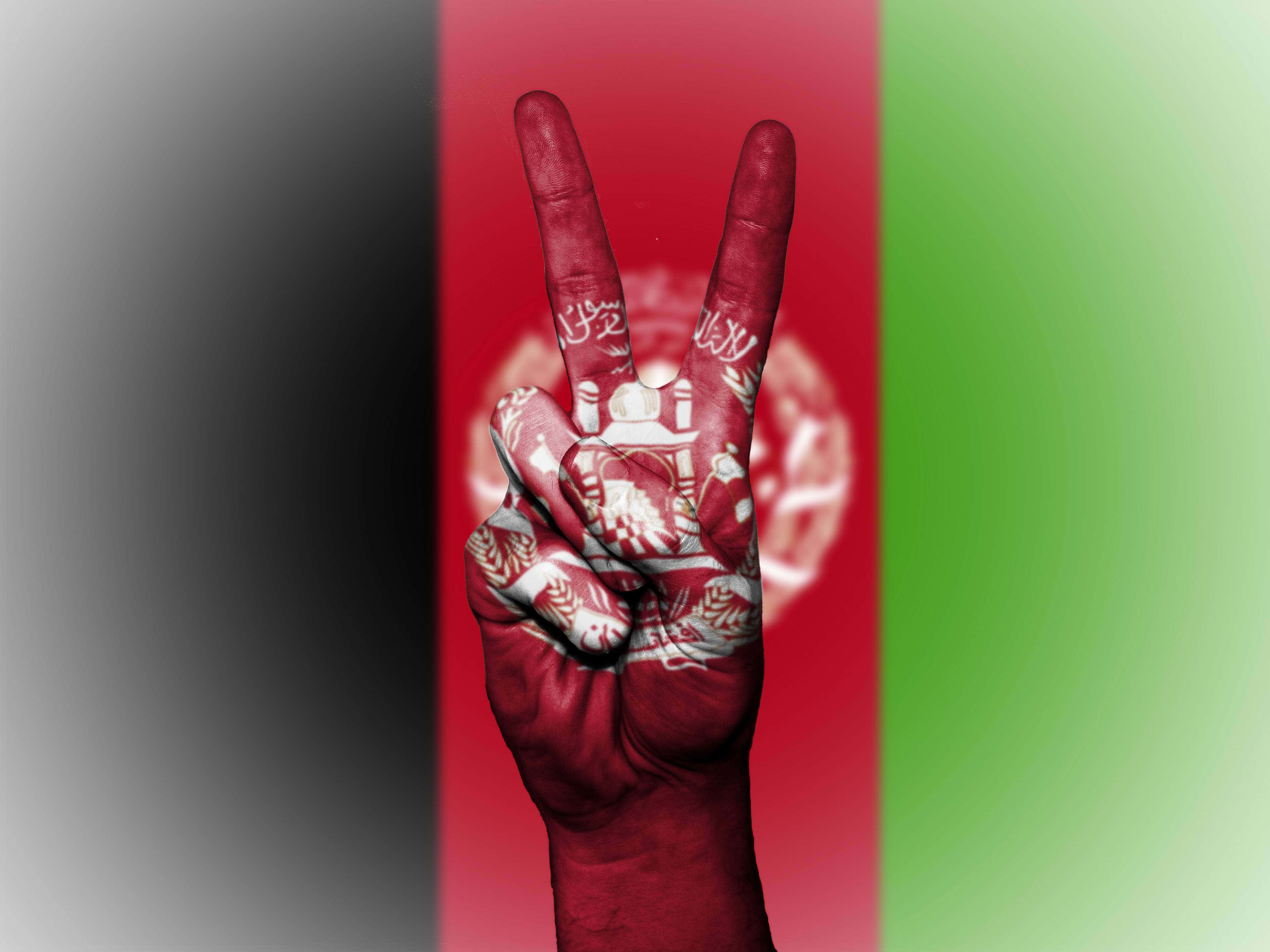 Afghanistan 桌布 壁紙 — 一隻塗有阿富汗國旗的手在模糊的國旗背景下做出和平手勢。
