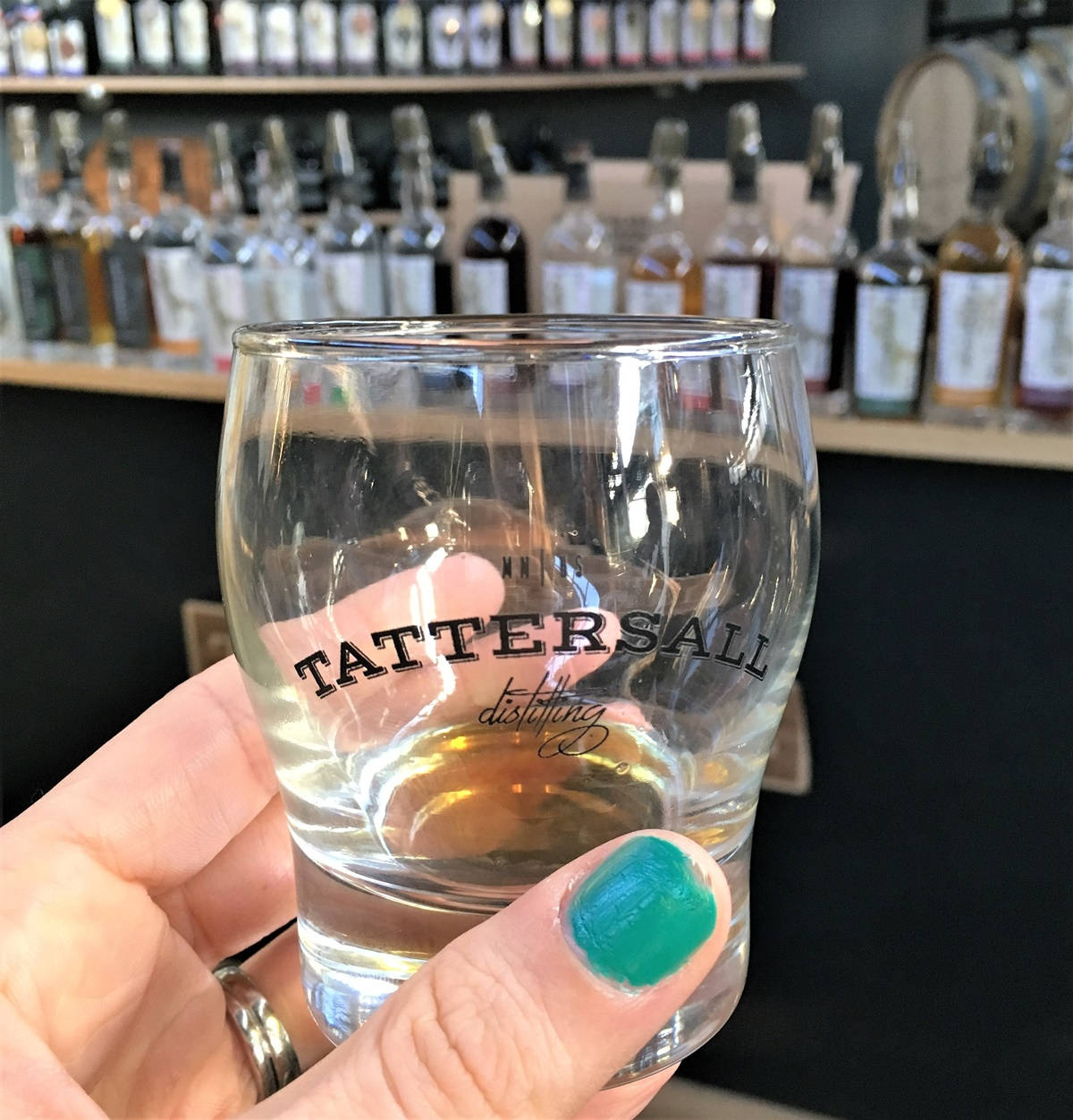 Drink 桌布 壁紙 — 一隻塗有青綠色指甲油的手，握著一個Tattersall Distilling玻璃杯，內含琥珀色液體，背景是威士忌酒瓶。