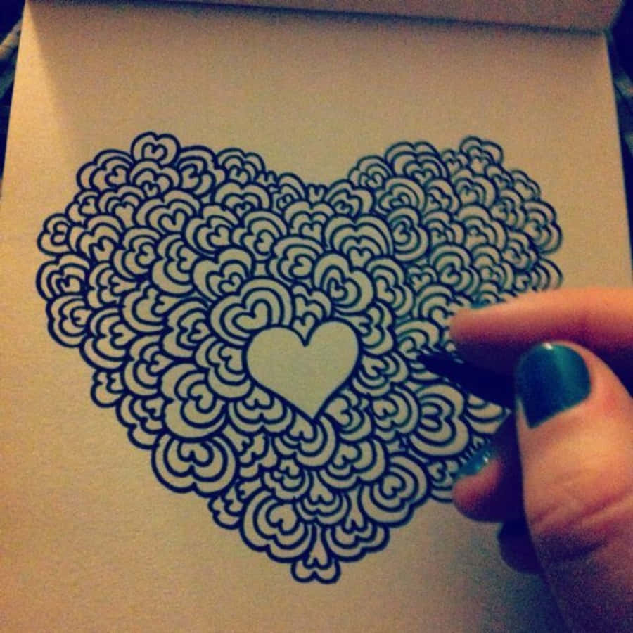 Heart Doodle 桌布 壁紙 — 一隻塗有青綠色指甲油的手，用細筆在米色紙上繪製一個精細的黑色心形曼陀羅。