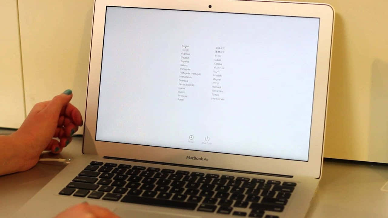 Mac 桌布 壁紙 — 一隻塗有青綠色指甲油的手懸浮在銀色MacBook Air附近，顯示語言選擇畫面。