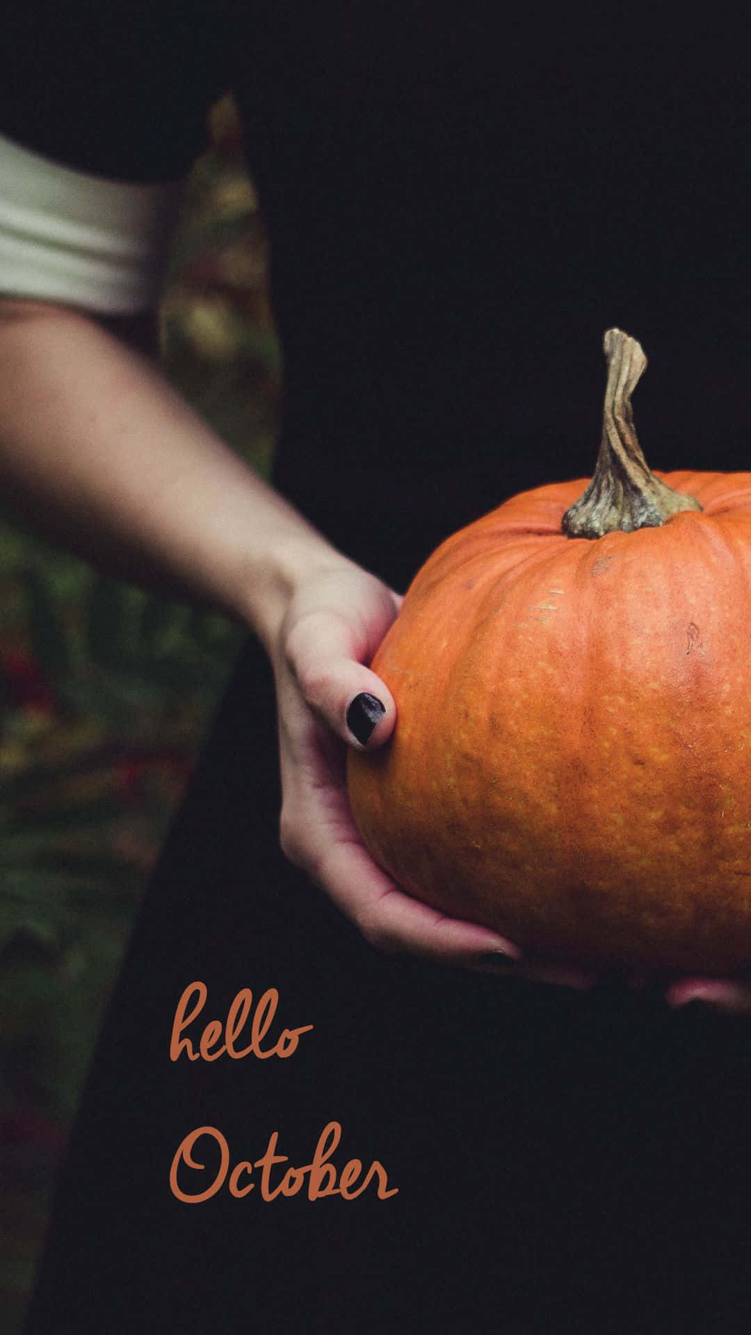 Hello October With Pumpkin 桌布 壁紙 — 一隻塗有黑色指甲油的手，在深色背景上輕輕托著一個鮮豔的橙色南瓜，上面有「hello October」文字。