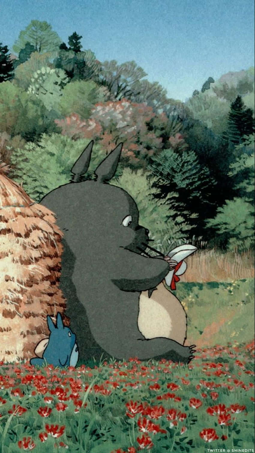 Aesthetic Ghibli 桌布 壁紙 — 一隻大型灰色龍貓坐在紅色花田裡，拿著一條白色絲帶，一隻藍色小生物從茅草屋頂後面探出頭來。