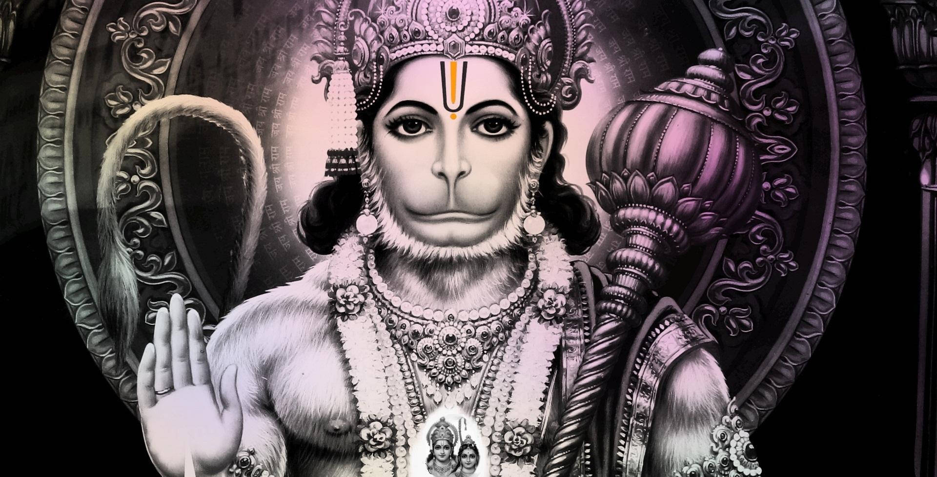 hanuman 4K HD 桌布 壁紙 — 一隻威嚴的猴神，裝飾著華麗的珠寶和皇冠，手持狼牙棒，在黑暗的裝飾背景前做出和平的手勢。