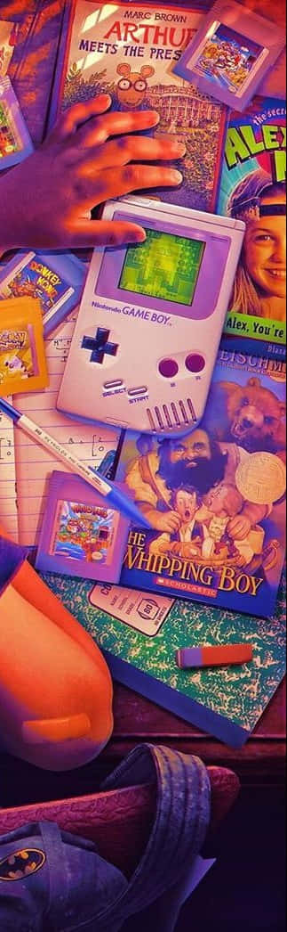 nostalgic 桌布 壁紙 — 一隻孩子的手拿著紫色 Game Boy，周圍是色彩繽紛的兒童書籍和學校用品，在溫暖的燈光下。