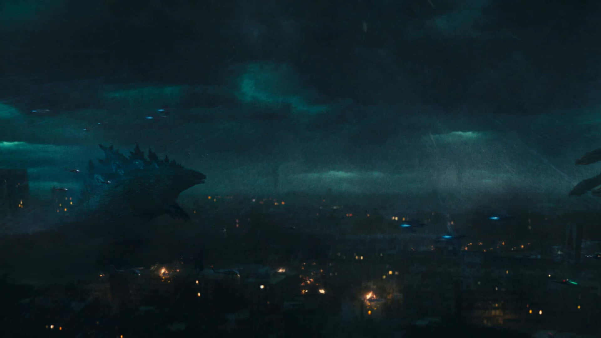 Godzilla City Destruction 桌布 壁紙 — 一隻巨大的哥吉拉在夜晚籠罩著被雨水浸濕的城市，下方有發光的青綠色雲朵和散落的街燈。