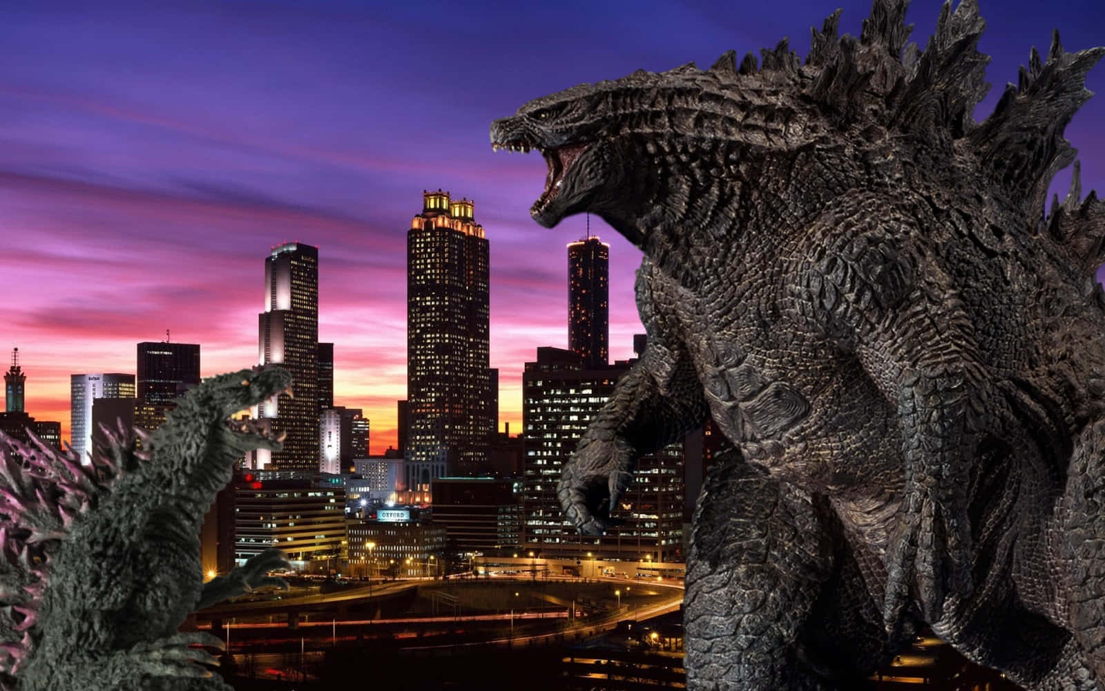Godzilla 2000 桌布 壁紙 — 一隻巨大的哥吉拉在黃昏時分，於紫色和橙色天空下，對著發光的城市景觀咆哮。