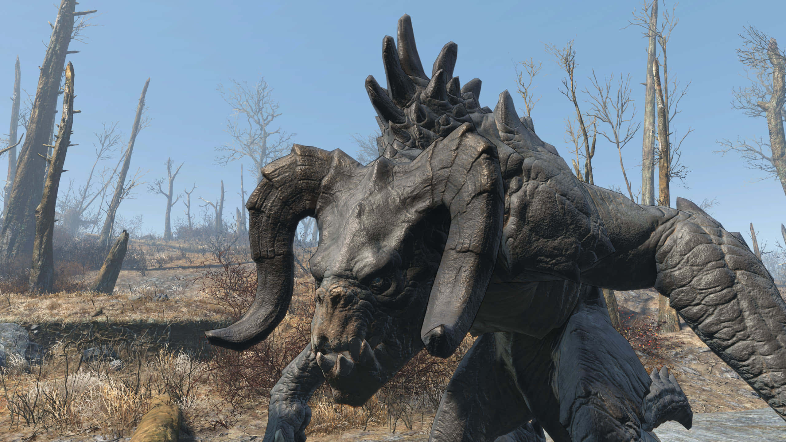 Deathclaw 桌布 壁紙 — 一隻巨大的有角野獸，披著裝甲般的皮膚，在晴朗藍天下荒蕪貧瘠的荒野中徘徊。