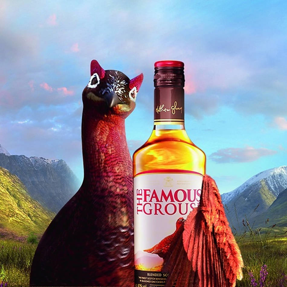 Whiskey 桌布 壁紙 — 一隻巨大的紅松雞站在一瓶 The Famous Grouse 威士忌旁邊，背景是日落時分的蘇格蘭山區景觀。