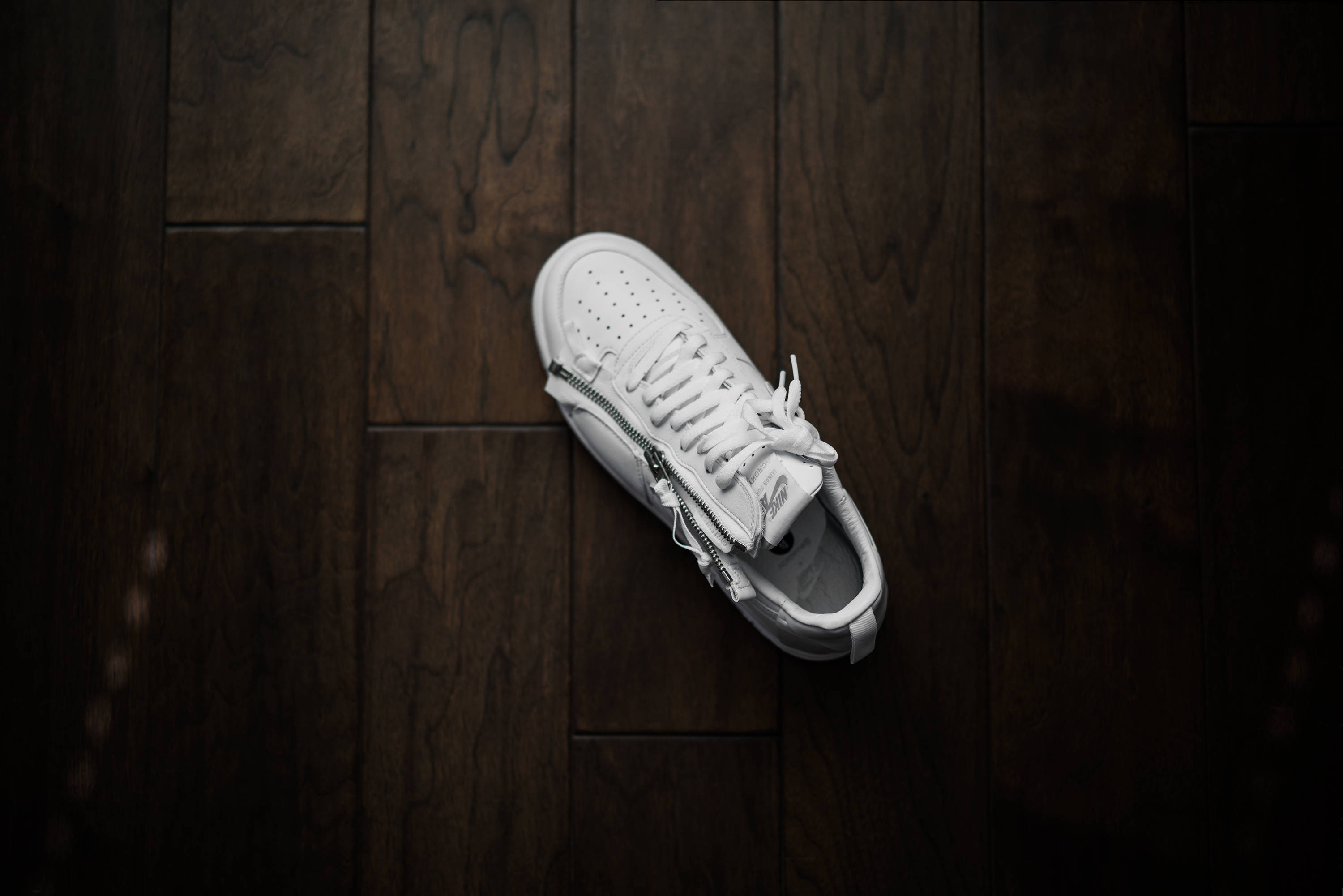 Nike 桌布 壁紙 — 一隻帶拉鍊細節的白色運動鞋放在深色木地板上，以極簡風格從上方拍攝。