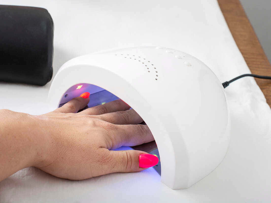 Manicure 桌布 壁紙 — 一隻帶有亮粉紅色指甲的手放在一個白色UV指甲烘乾機內，發出紫色光線，置於乾淨的白色表面上。