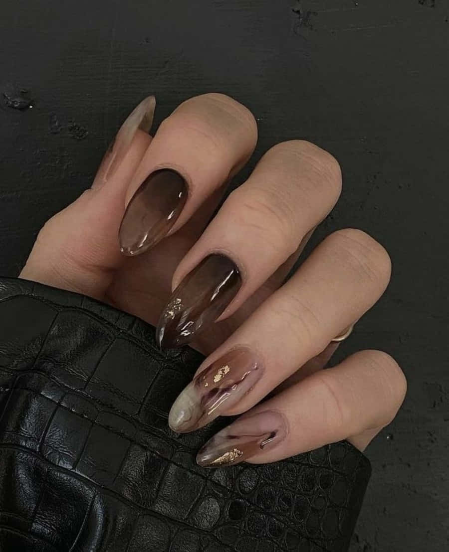 Nail Polish 桌布 壁紙 — 一隻帶有光澤漸層棕色指甲並飾有金箔點綴的手，放在黑色鱷魚紋表面上。