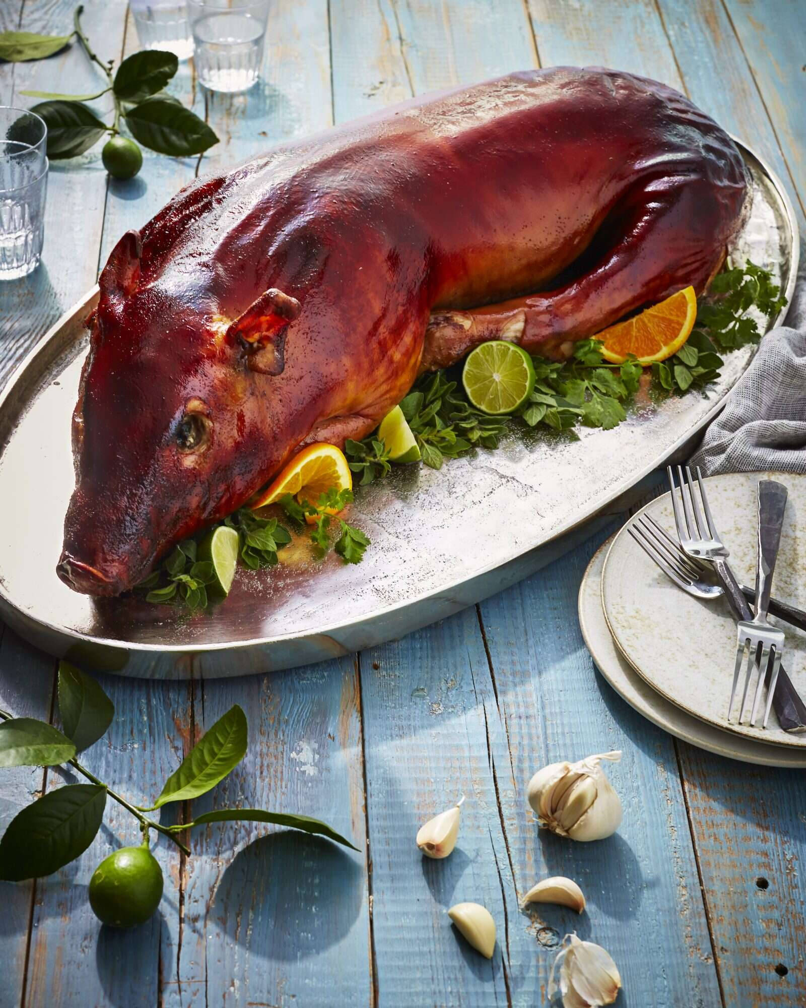 Pig 桌布 壁紙 — 一隻帶有光澤焦糖化外皮的整隻烤豬，放在銀盤上，飾以柑橘和香草，置於質樸的藍色木桌上。