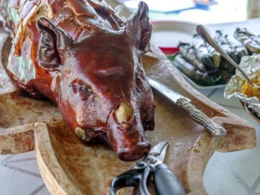 Pig 桌布 壁紙 — 一隻帶有光澤焦糖化外皮的整隻烤豬，放在木盤上，旁邊有餐具和配菜。