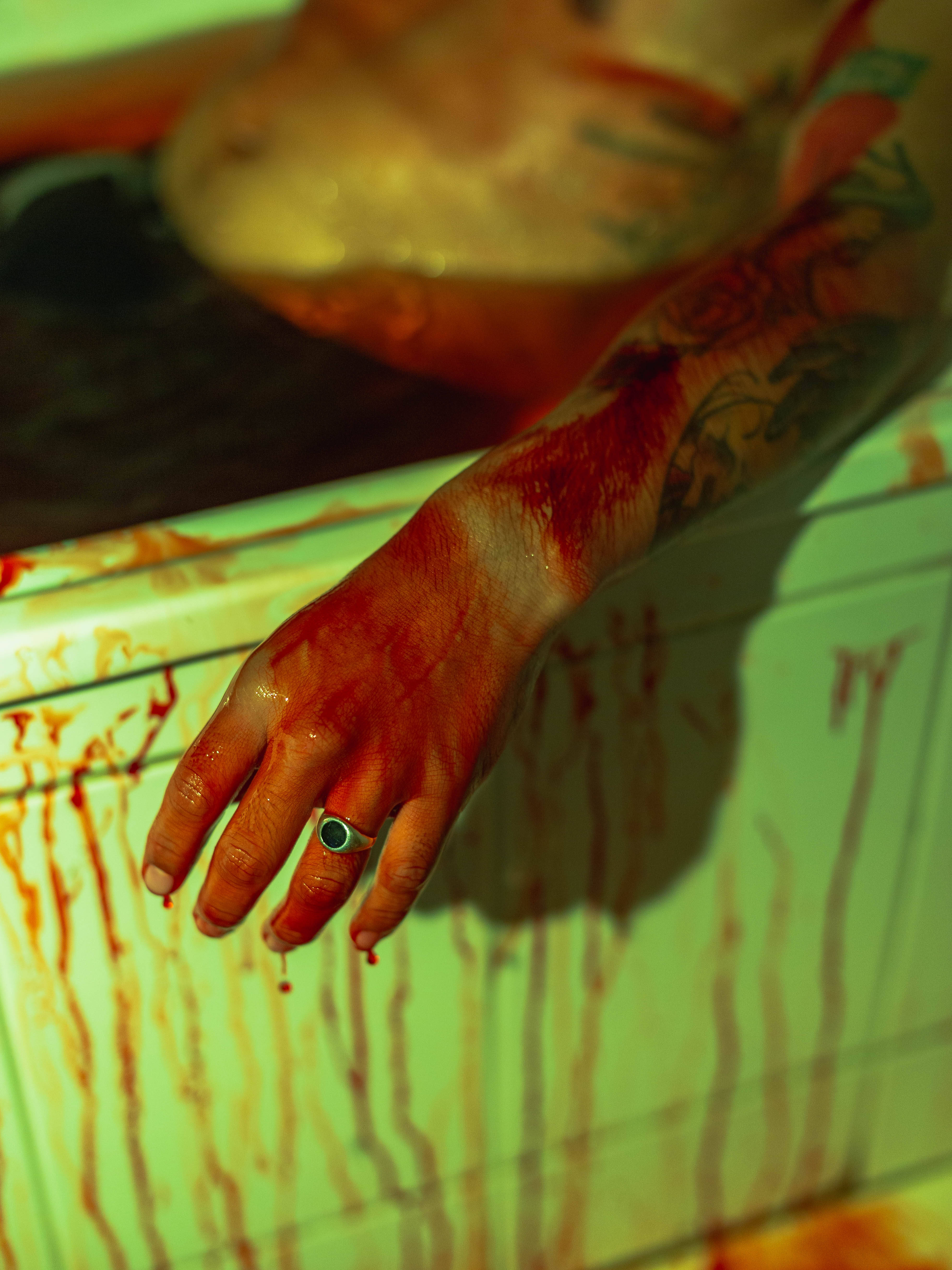 Blood 桌布 壁紙 — 一隻帶有刺青和戒指的血淋淋的手，放在沾滿滴落紅色液體的綠色瓷磚表面上。