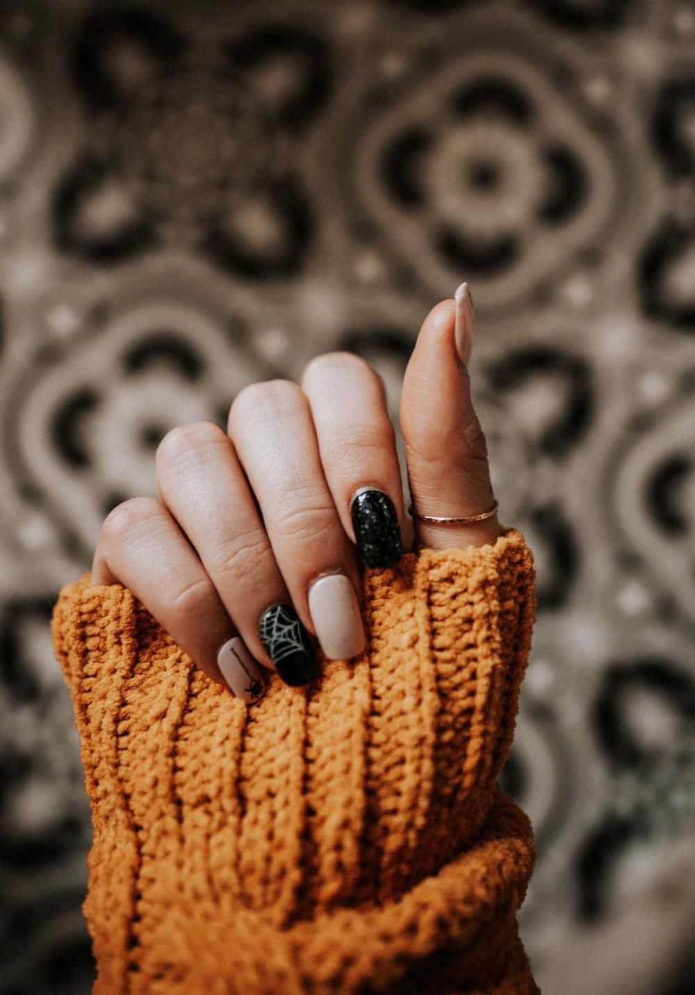 Cute Nails 桌布 壁紙 — 一隻帶有時尚黑色和米色指甲的手從舒適的橙色針織袖中伸出，背景為圖案背景。